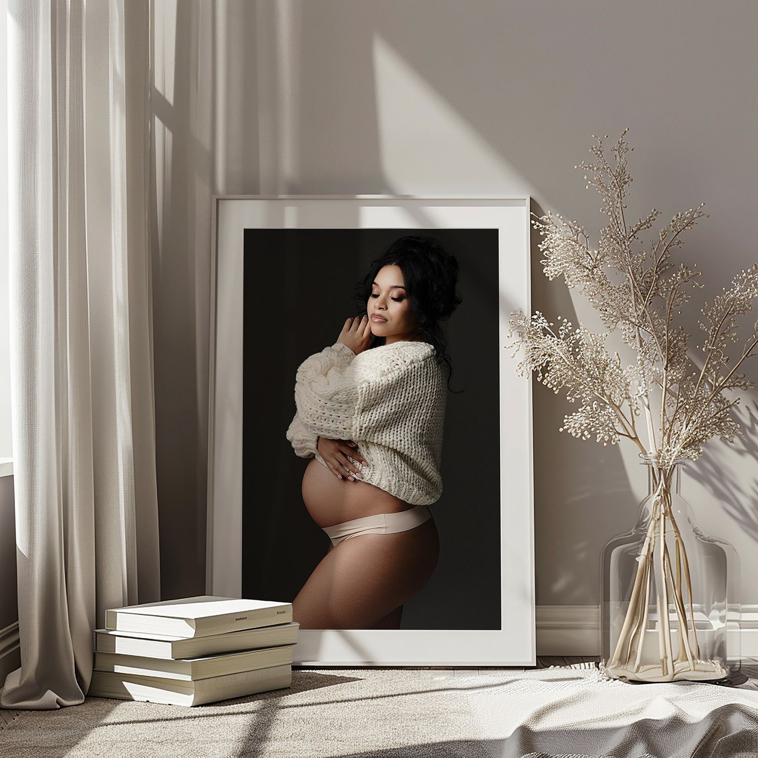 Elegant framed maternity portrait of a pregnant woman in a white sweater, displayed in a cozy room with dried flowers.