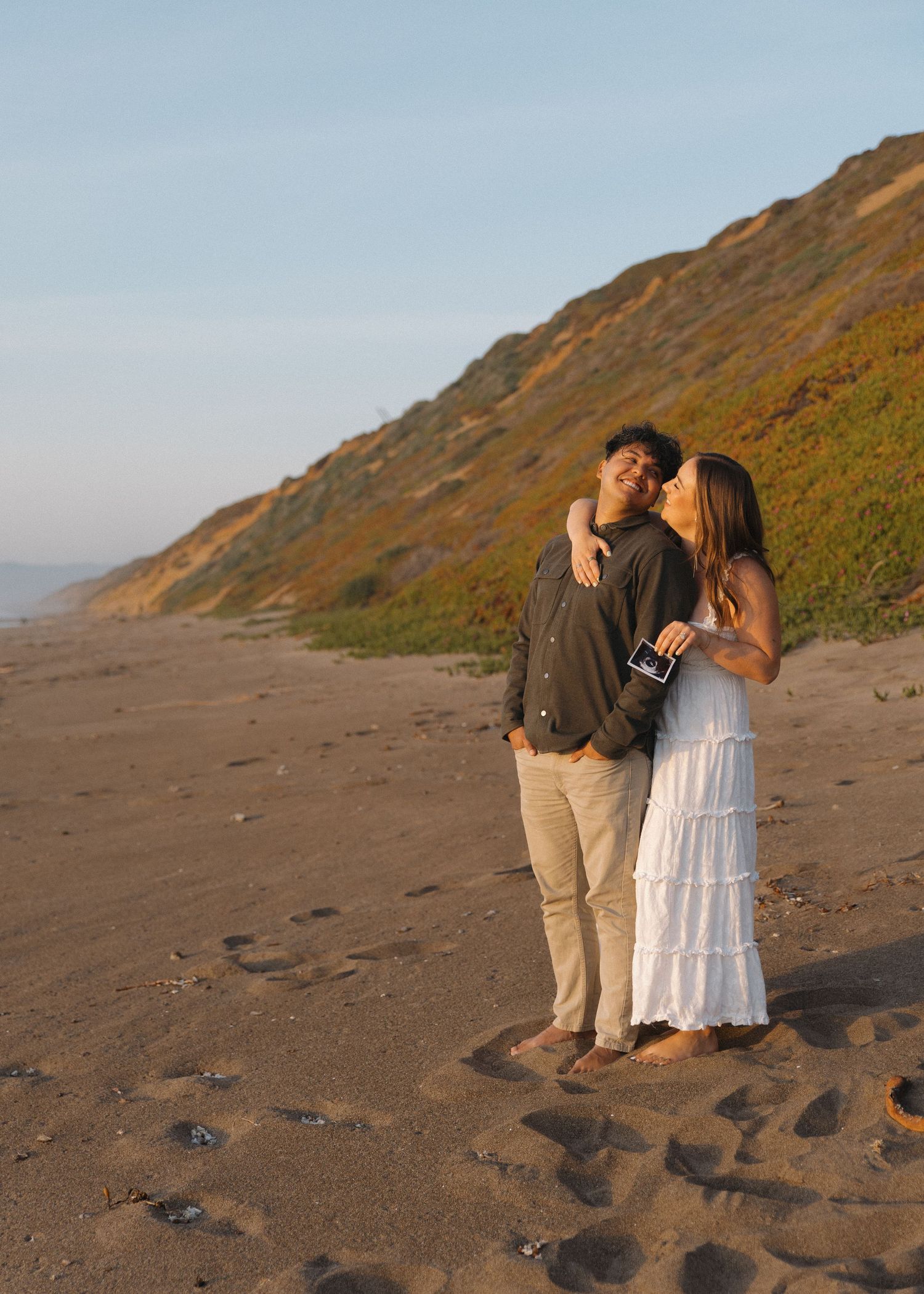 A romantic scene of a couple holding their ultrasound at sunset along Montana De Oro Beach in Los Osos, California.