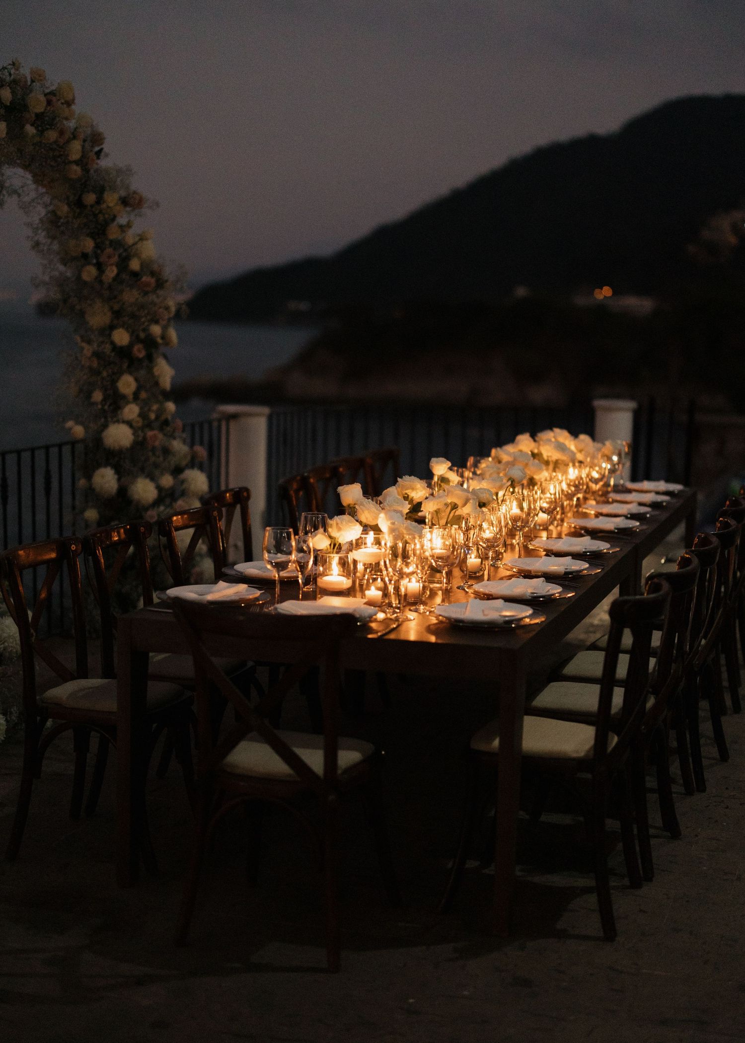 A candlelit outdoor wedding reception dining table setup at dusk with ocean views in Puerto Vallarta, Mexico.