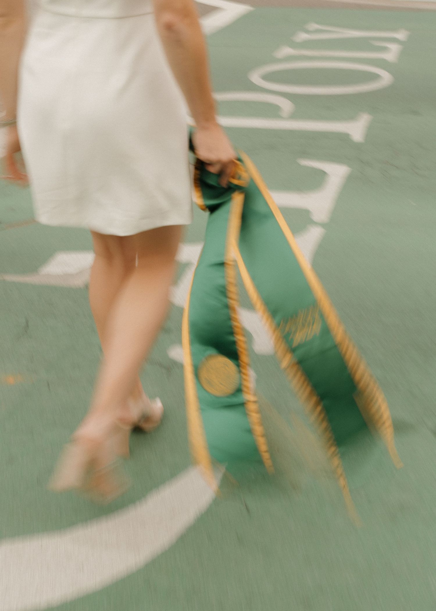 A blurry image of a Cal Poly San Luis Obispo Graduate walking on the campus cross walk holding her stole.