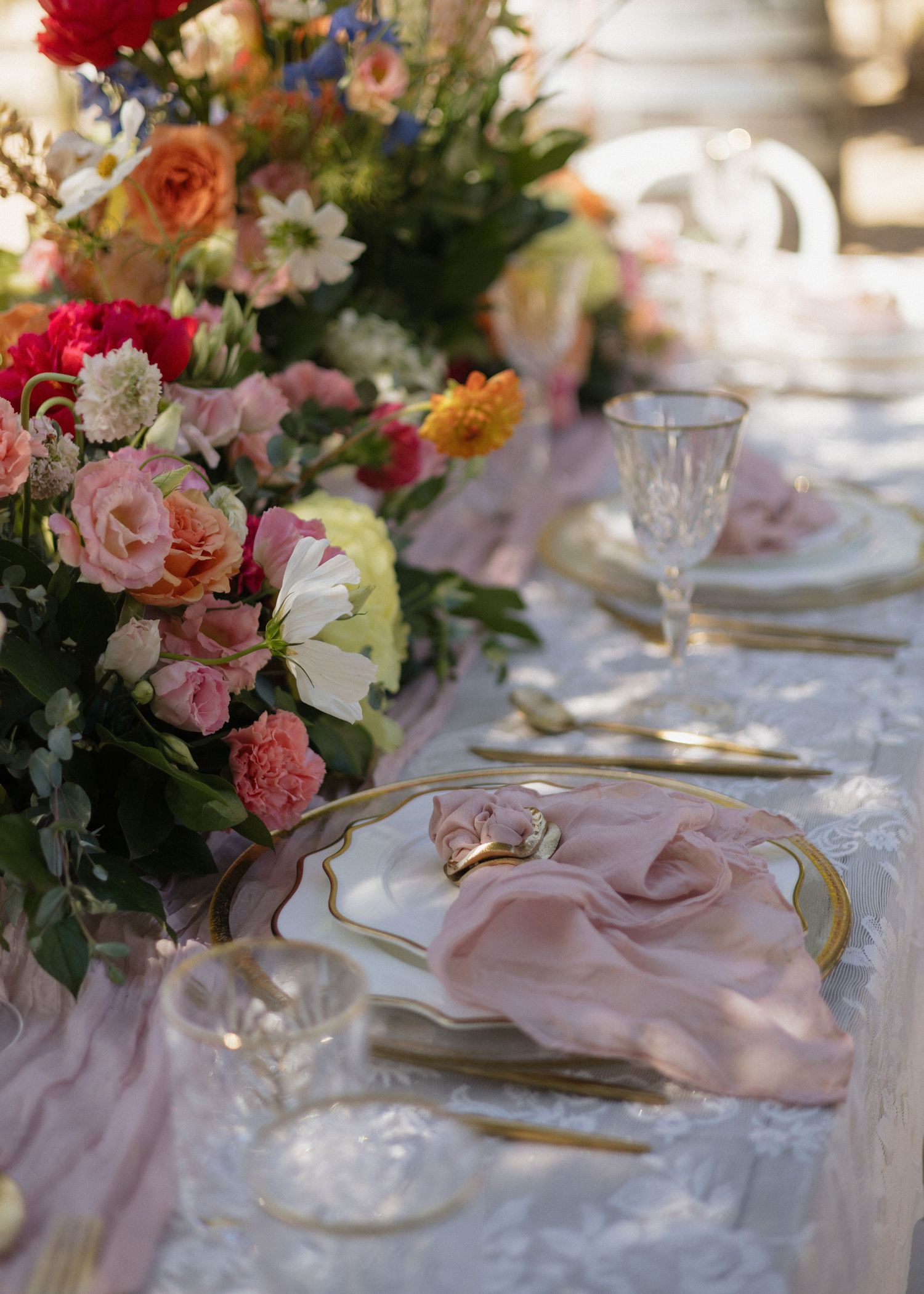 Elegant wedding table setting with pink napkins, crystal glassware, and fresh floral centerpieces on white tablecloth.