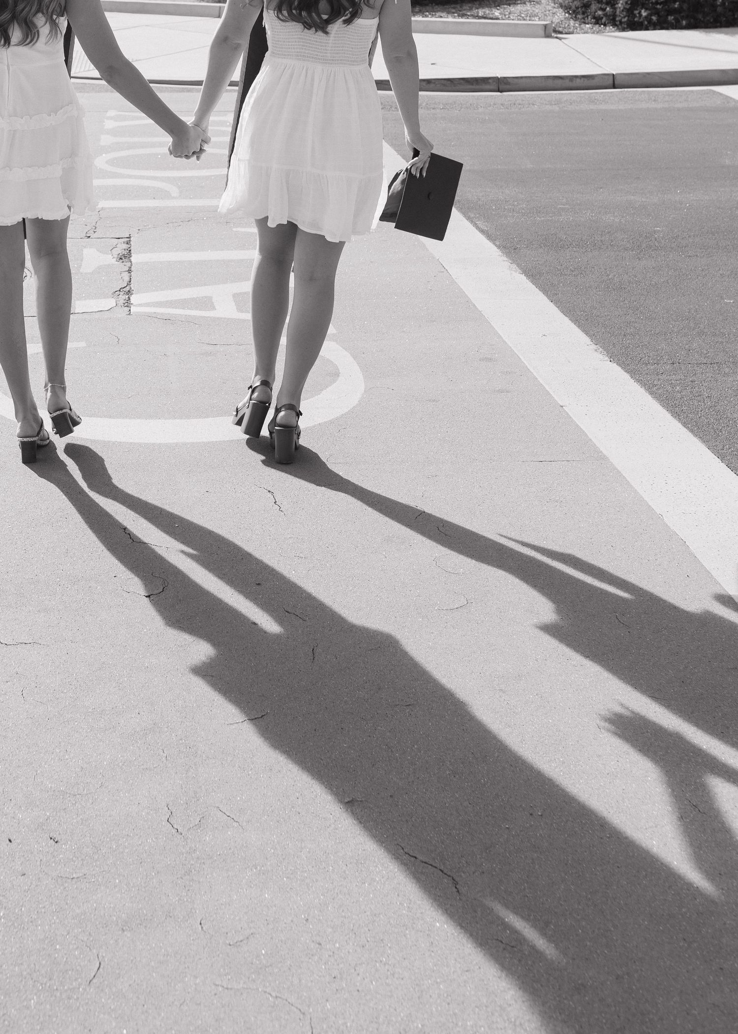 Two Cal Poly San Luis Obispo graduates hand in hand walking down the campus crosswalk holding their caps.