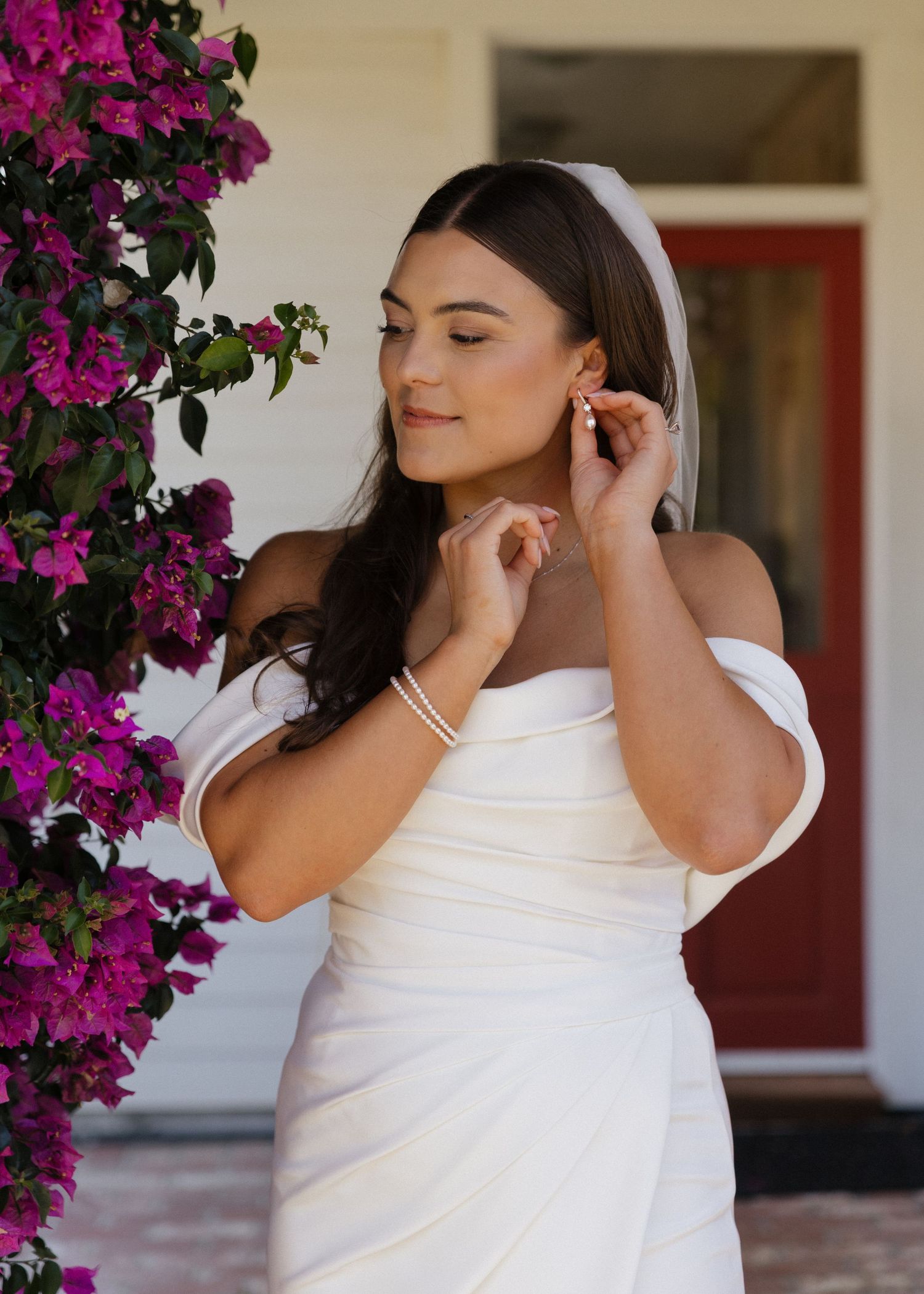 A bride fixing her earring elegantly against a backdrop of vibrant magenta bougainvillea flowers.