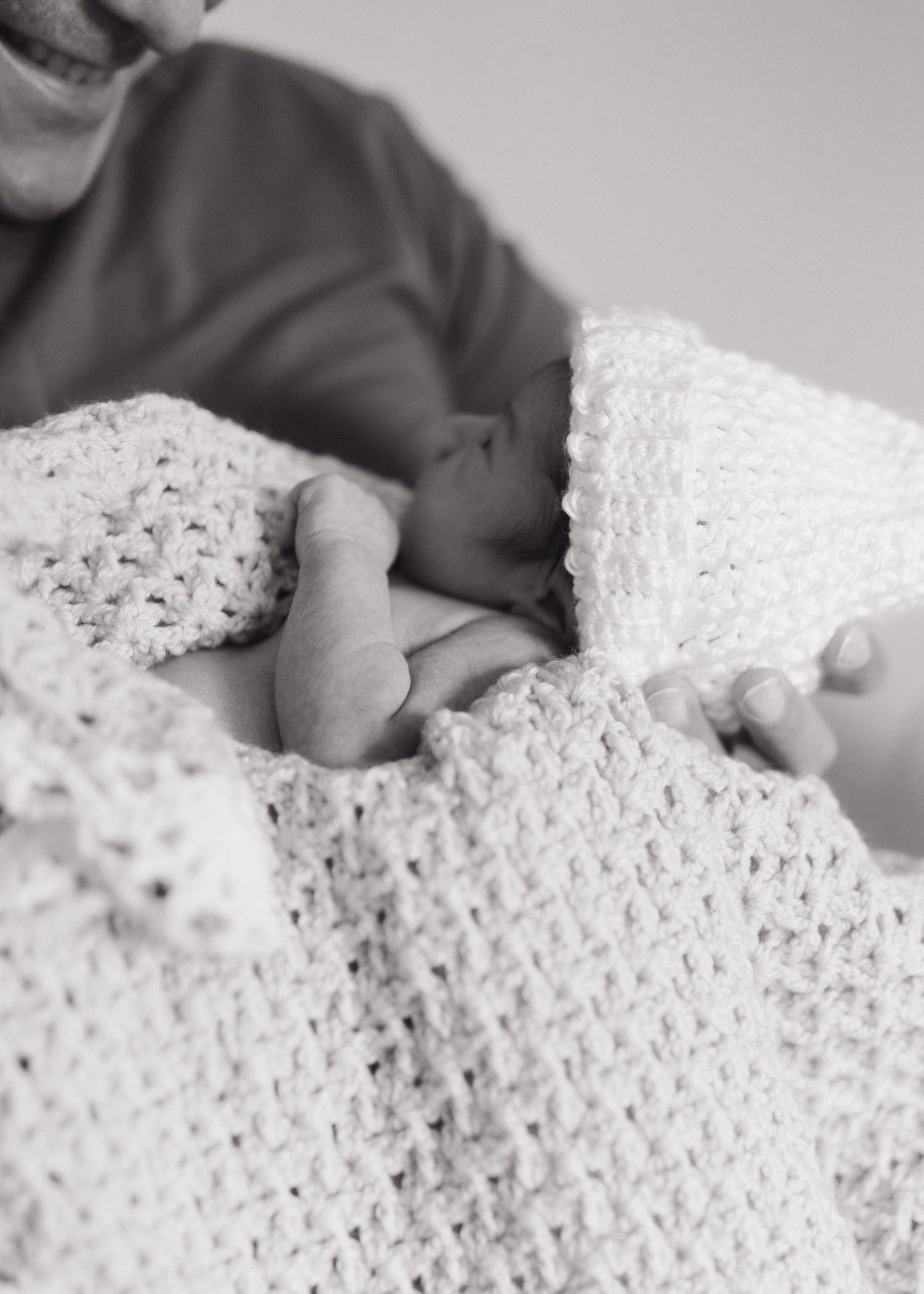 A tiny newborn foot peeks out from under a cozy white knitted blanket in a black and white photograph.
