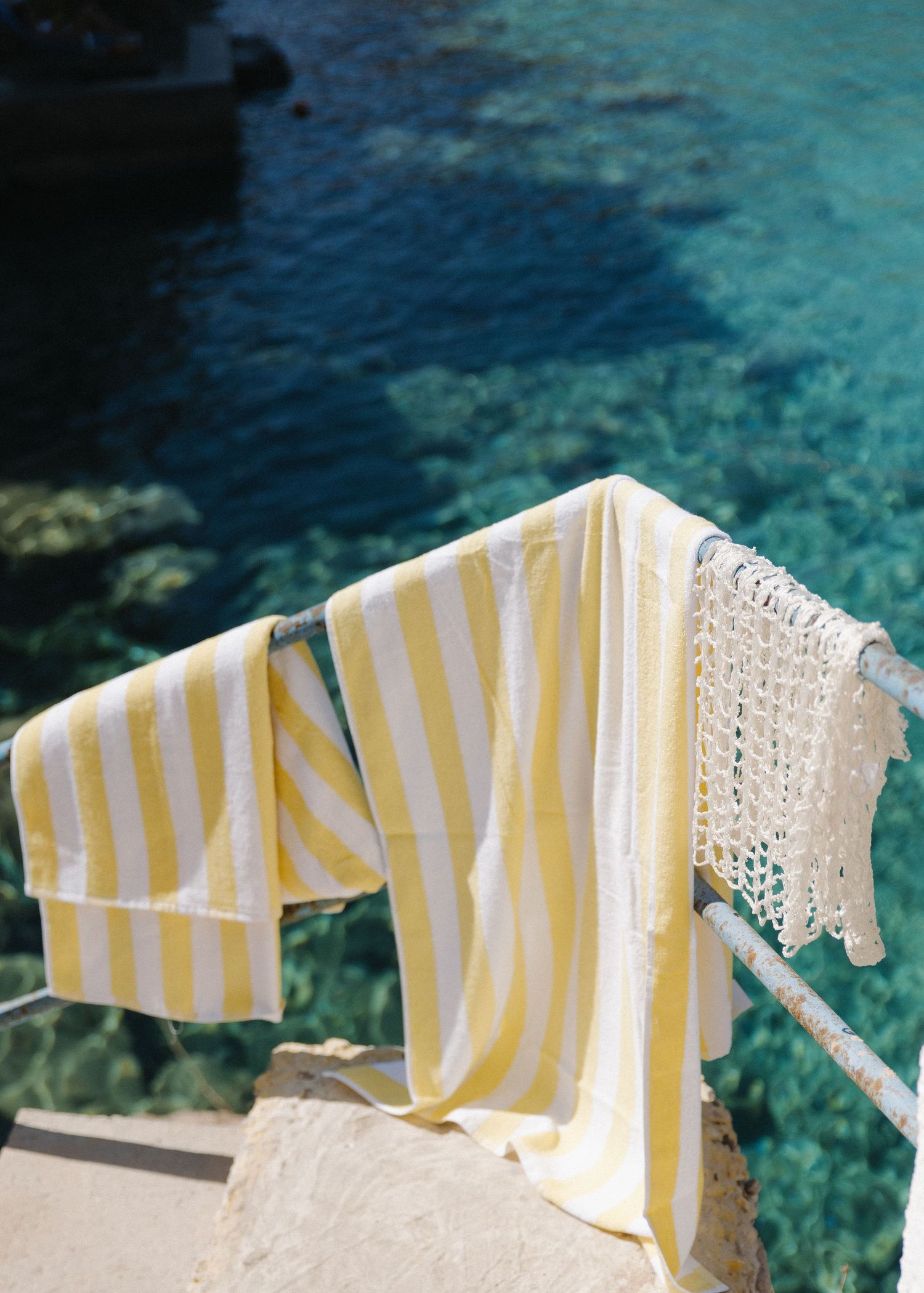 Yellow and white striped towels hanging to dry on a railing overlooking crystal clear turquoise Mediterranean waters.