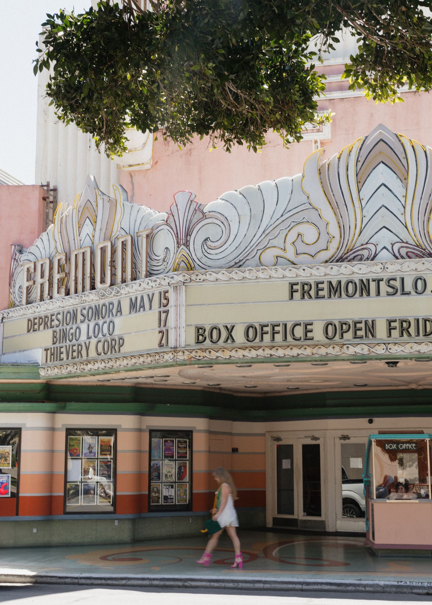 A Cal Poly San Luis Obispo graduate walking in front of the entrance of the historic Fremont Theater with ornate architectural details.