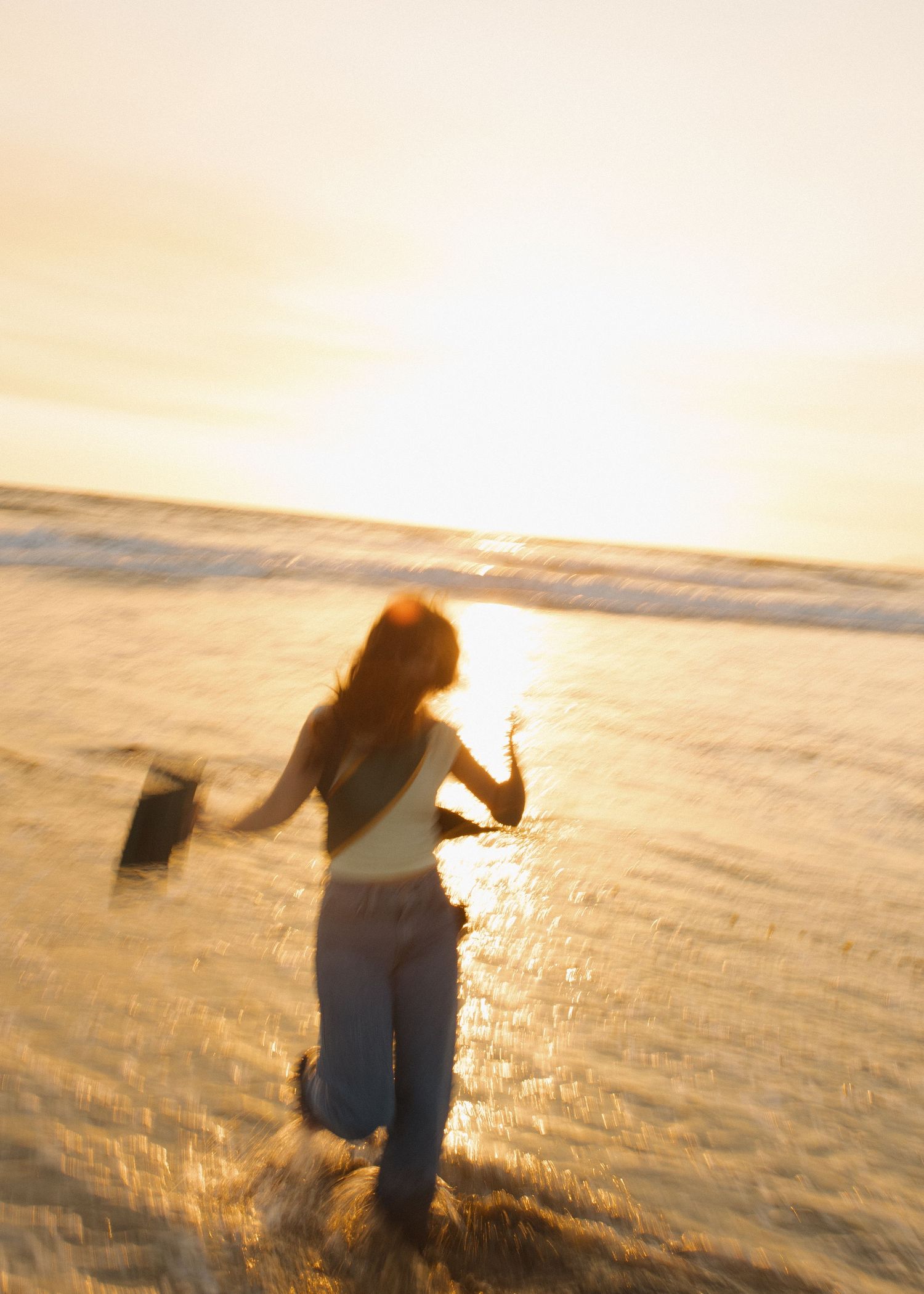 A blurry silhouette of a Cal Poly San Luis Obispo graduate dancing joyfully at Morro Bay beach in California during golden hour.