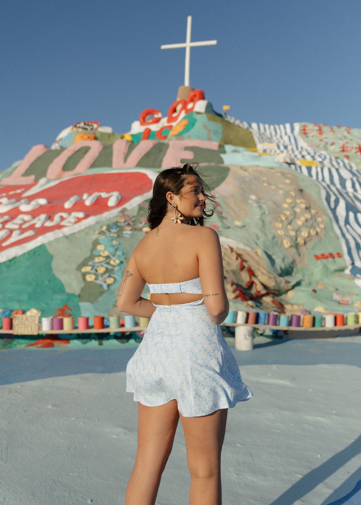 A graduate in a blue and white dress poses at Salvation Mountain, a colorful outdoor art installation in the California palm desert.