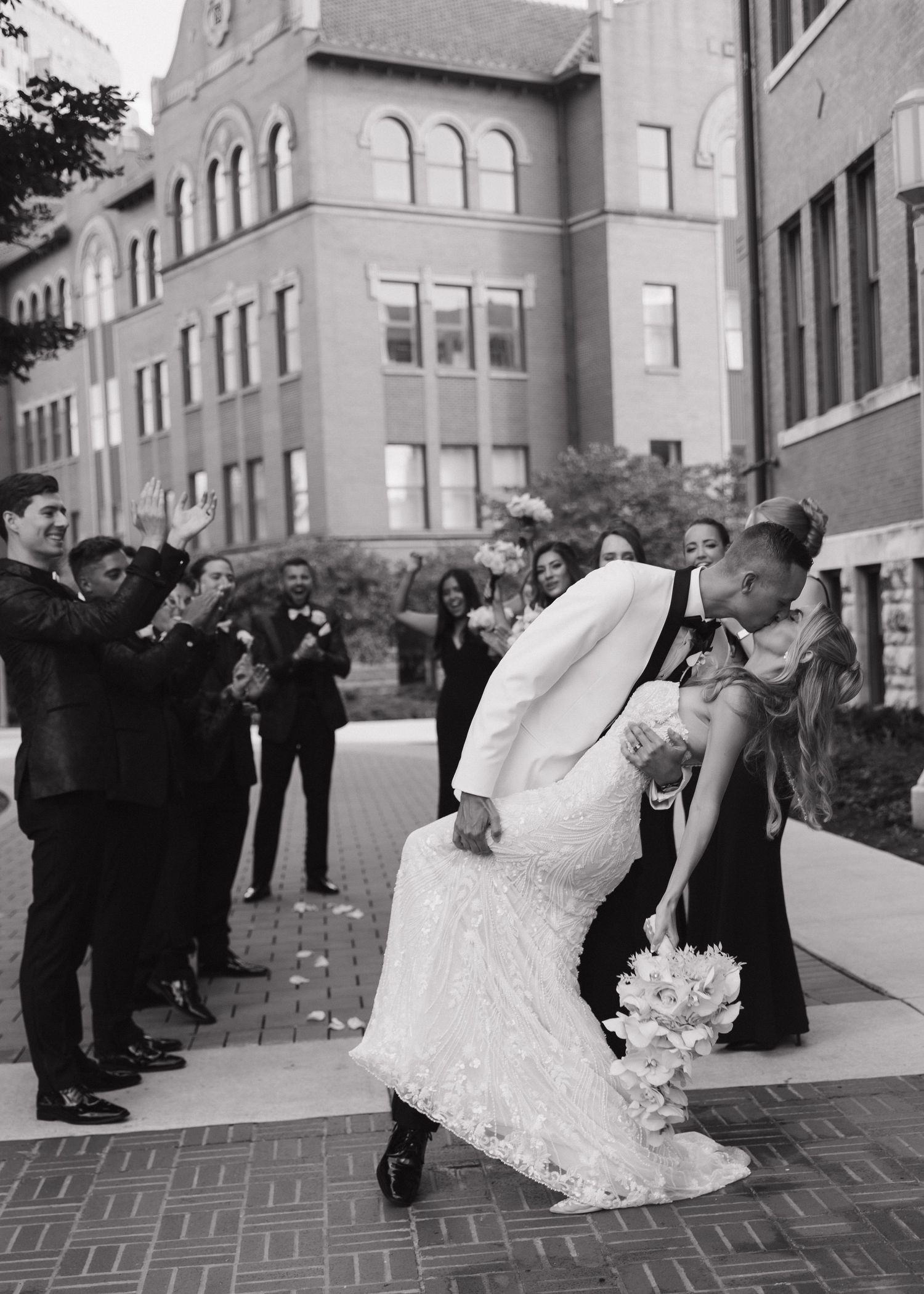 Bride and groom in a dip kiss outside Loyola University in Chicago, Illinois with their wedding party lined up behind them.