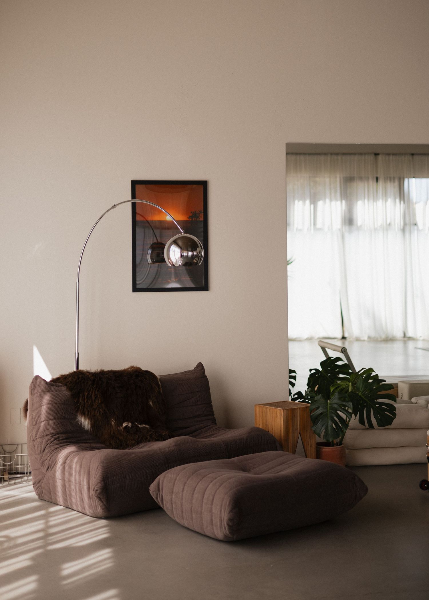 A modern pilates studio interior with brown sectional sofa, potted plants, and natural light streaming through sheer curtains.