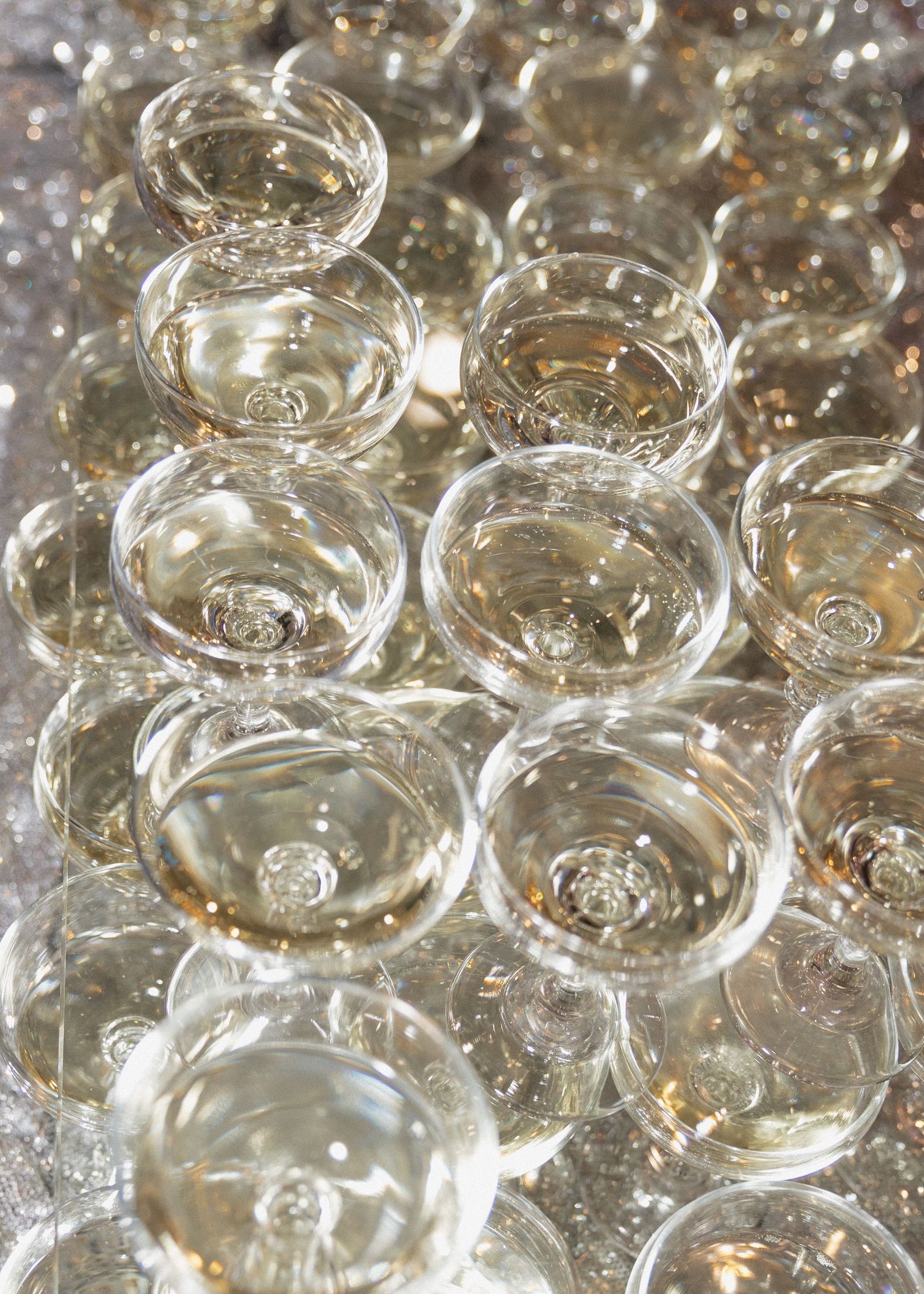 Multiple champagne glasses filled with sparkling wine arranged in rows creating a reflective pattern.