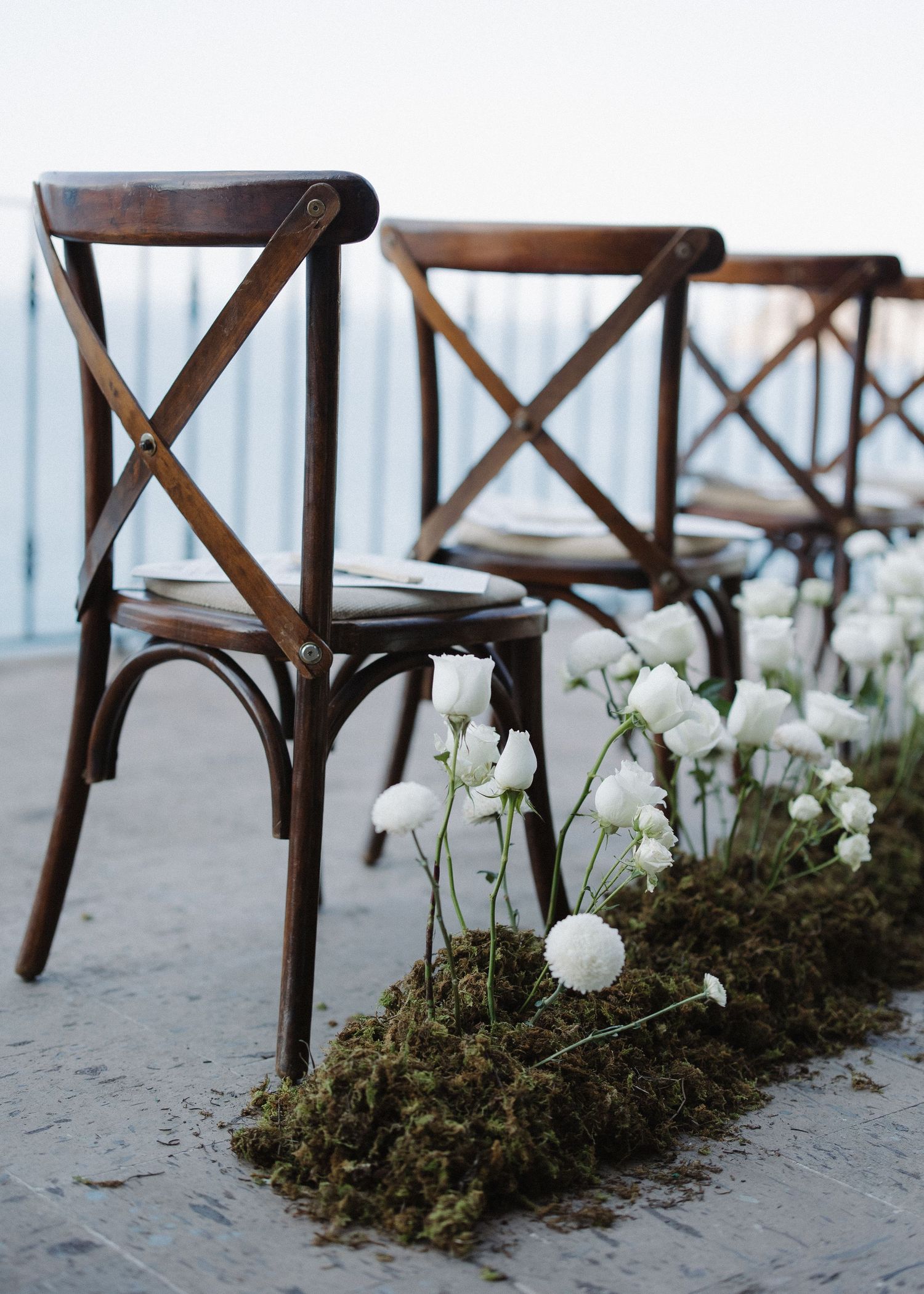White ranunculus flowers line an aisle of rustic wooden cross-back chairs at an elegant beach wedding in Puerto Vallarta, Mexico.