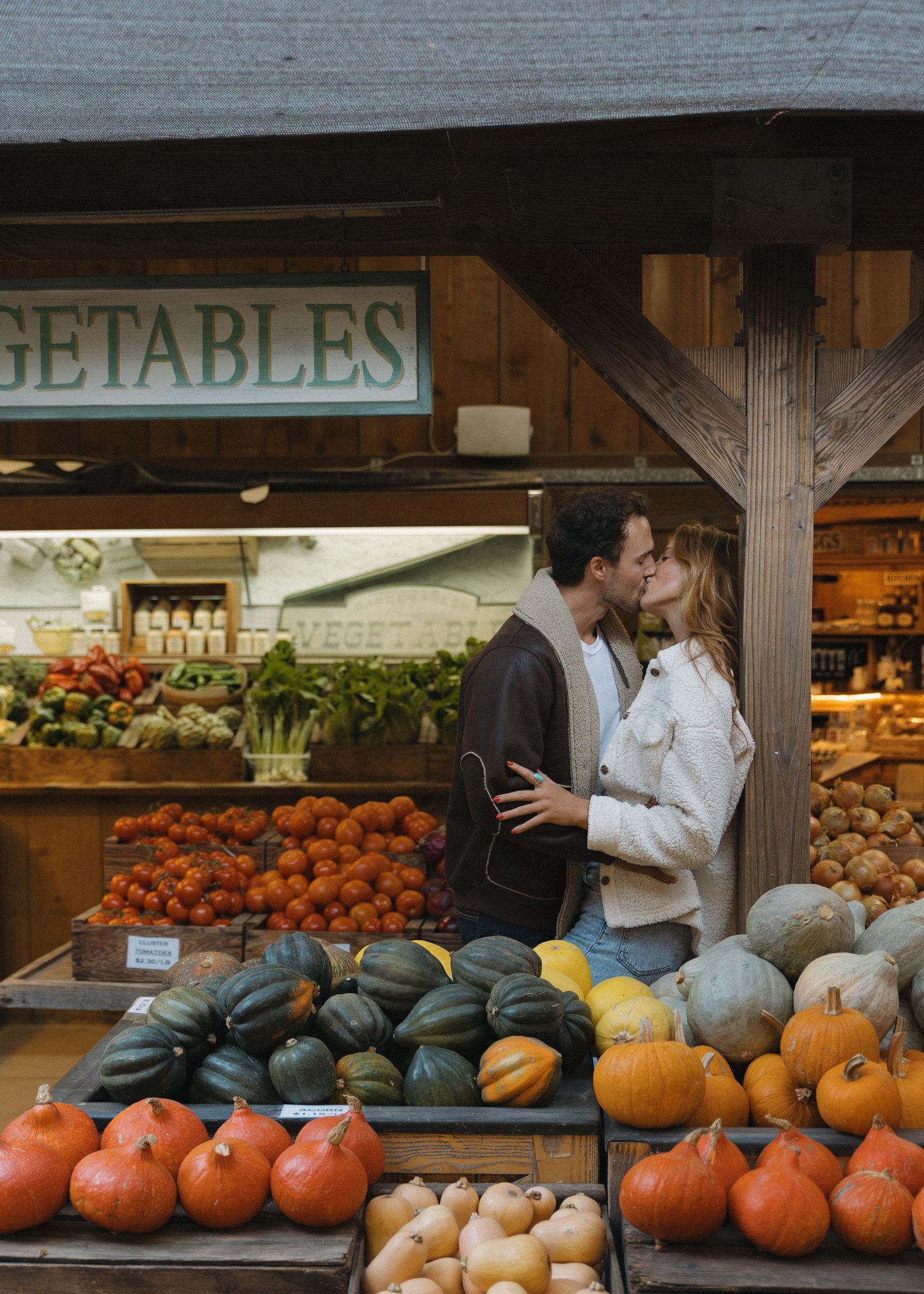 A couple kissing in a market produce stand with many autumn vegetables around at Avila Valley Barn in California.