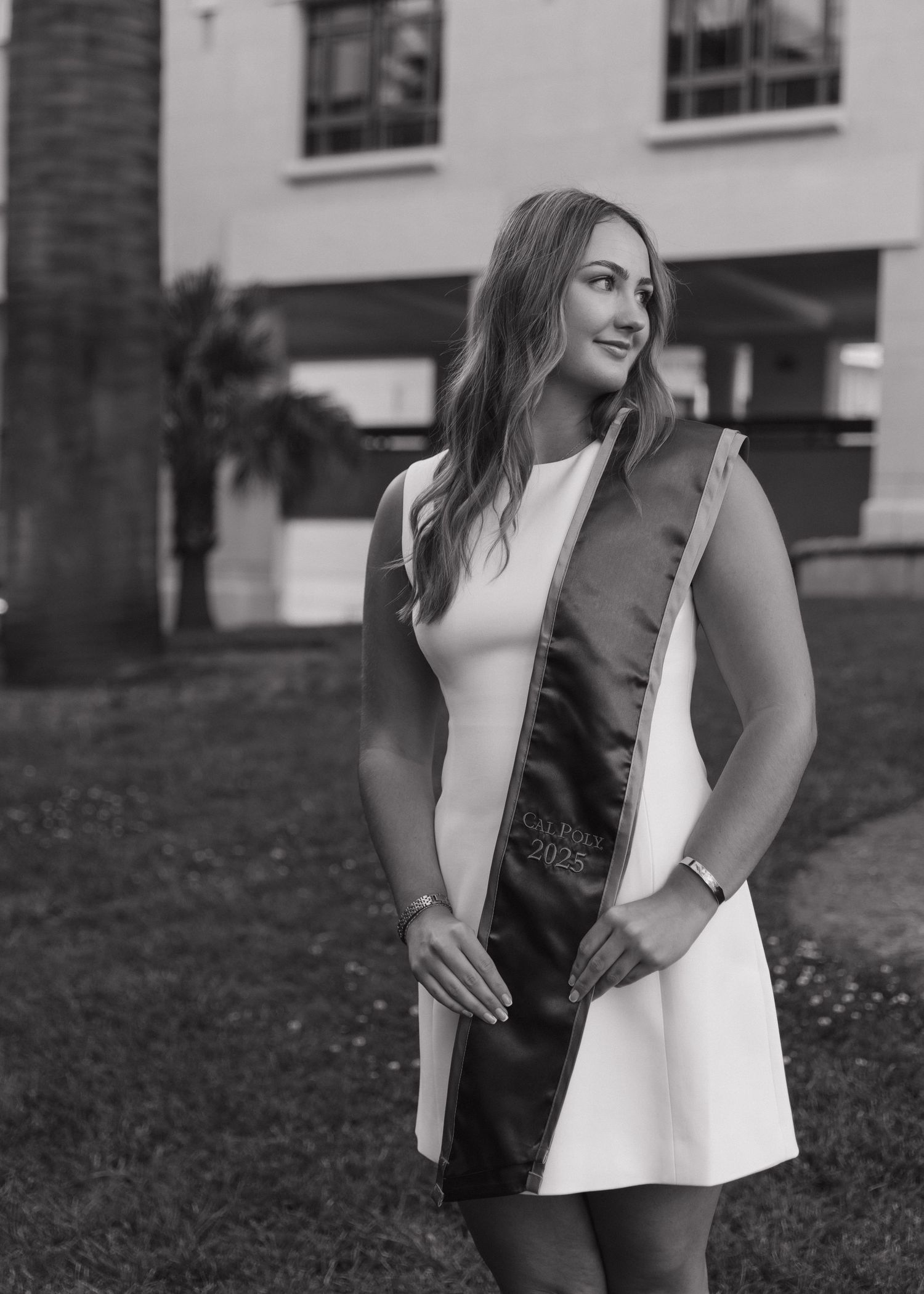 A black and white photo of a Cal Poly San Luis Obispo graduate posing outside the Orfalea College of Business.