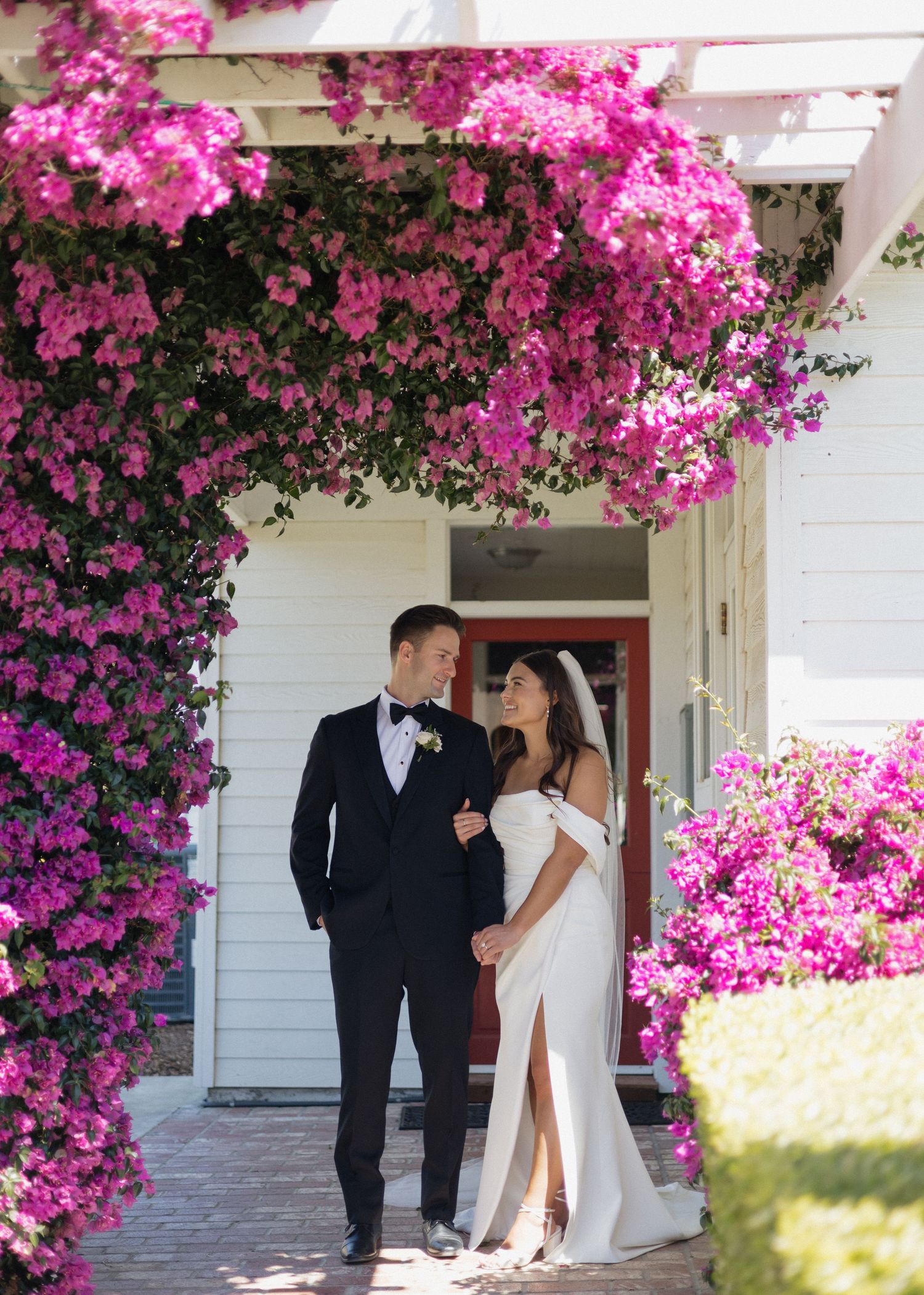 A romantic wedding portrait under pink bougainvillea flowers against the white house at Higuera Ranch in San Luis Obispo, California.