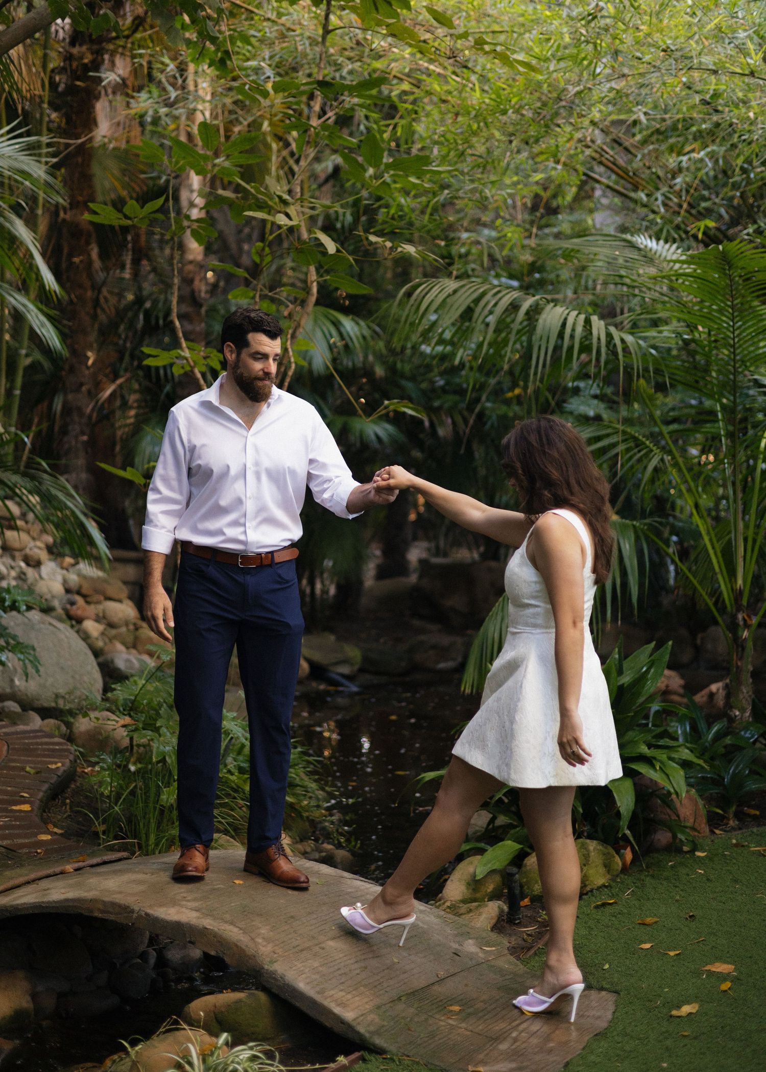 A couple walking across a stone bridge in a lush tropical garden at Hartley Botanica with greenery surrounding them in Camarillo, California