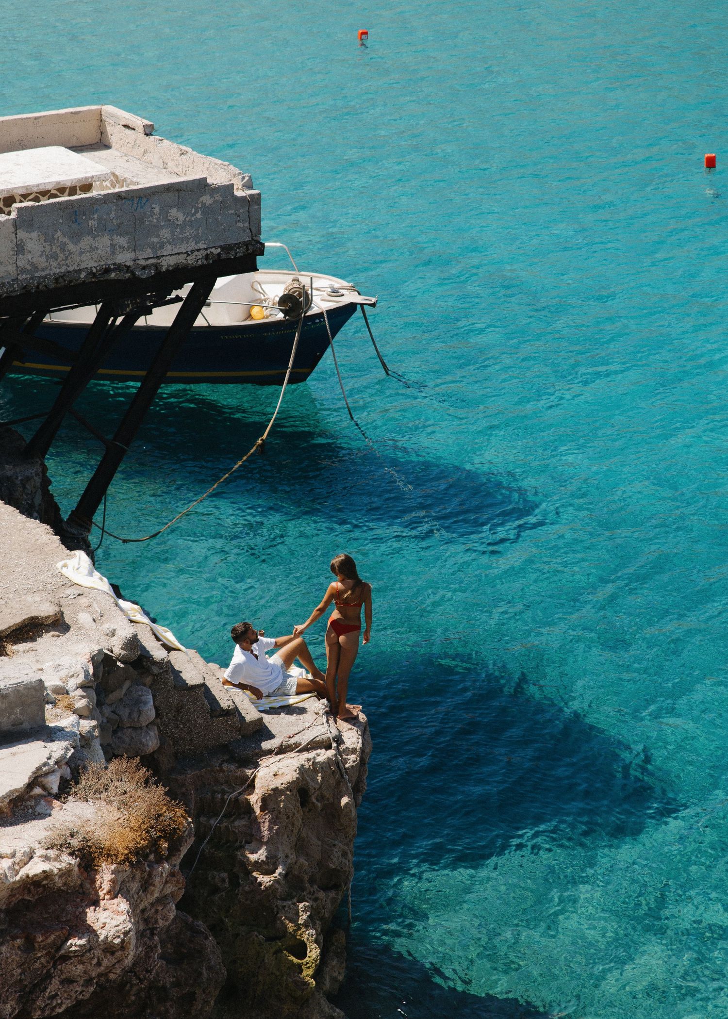A couple holding hands while cliff jumping into crystal clear turquoise Mediterranean waters on a sunny summer day in Milos, Greece.