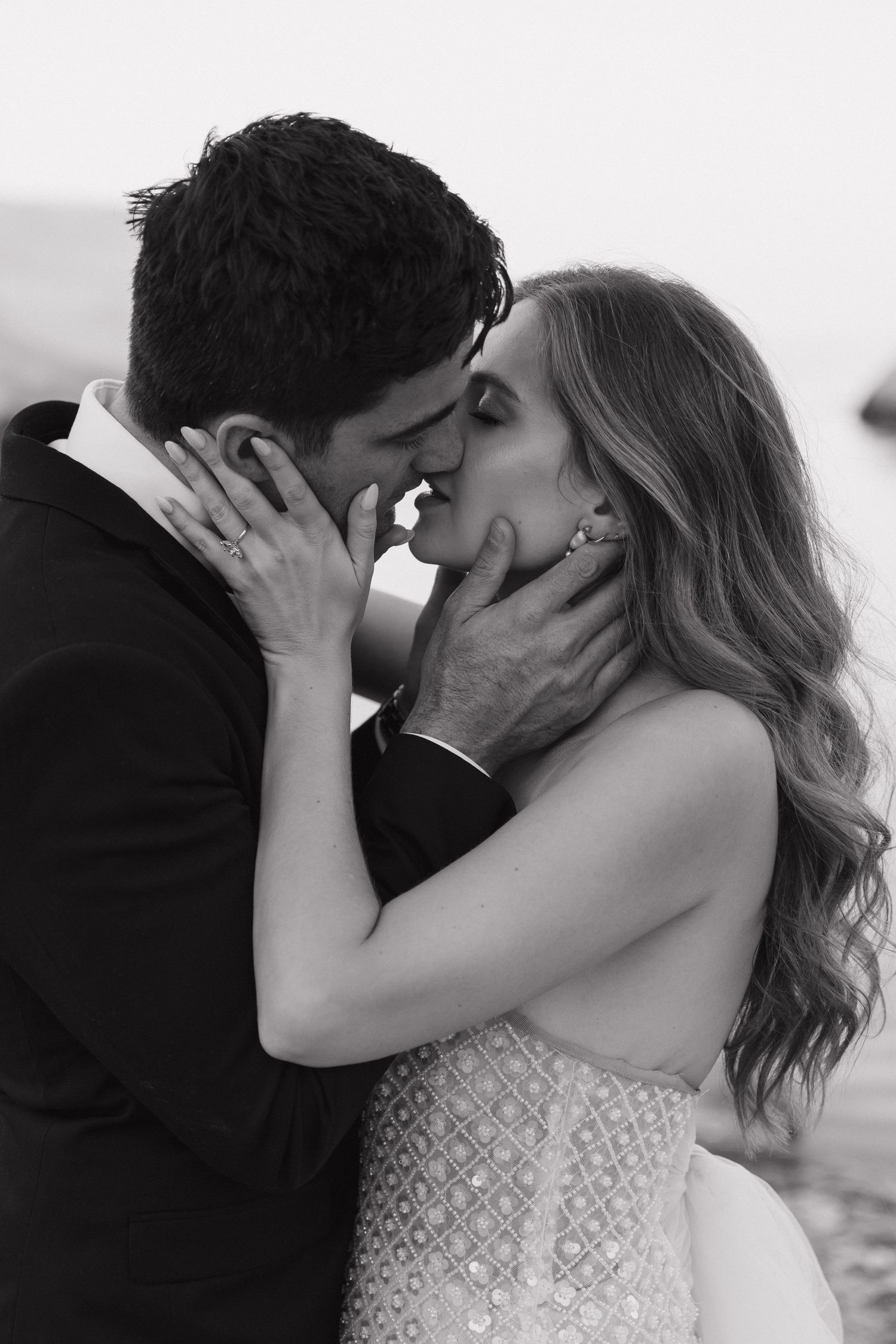 A romantic black and white photograph showing a bride and groom sharing an intimate kiss on the beach in Milos, Greece.