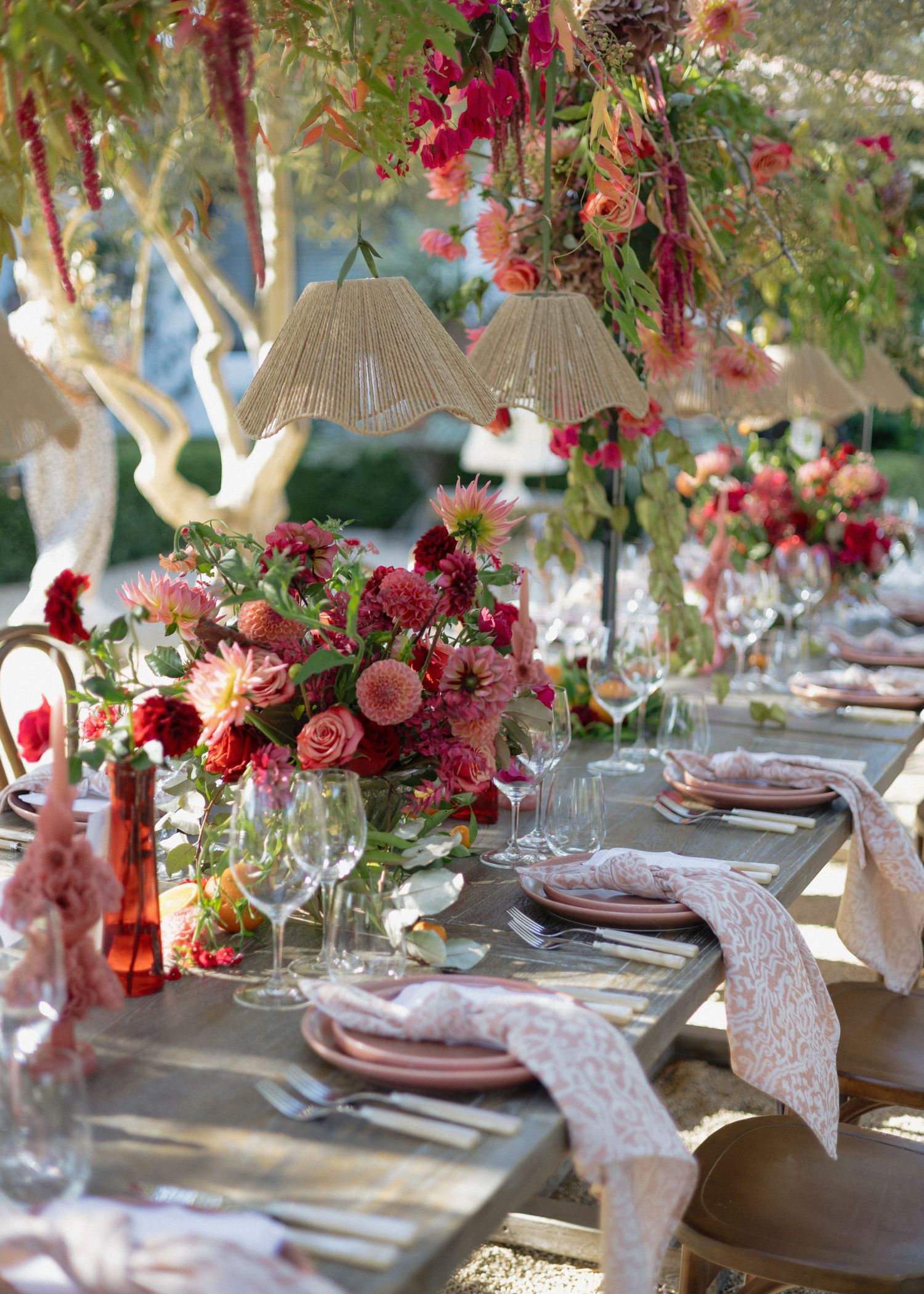 Elegant wedding table setting with deep red floral arrangements and crystal glassware on a rustic wooden table.