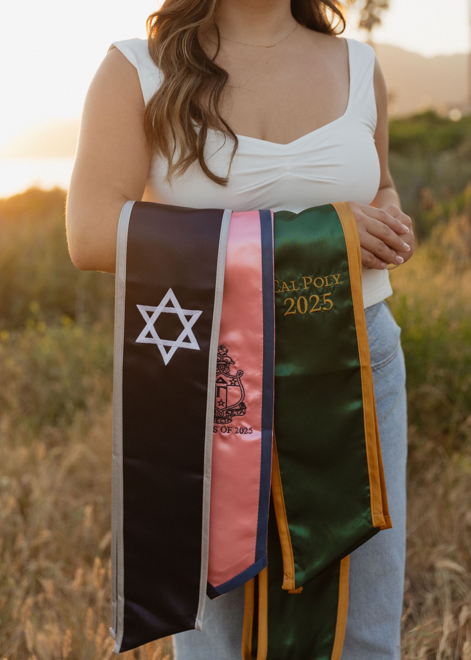 Cal Poly San Luis Obispo Graduation stoles held against a golden sunset in Shell Beach, California.