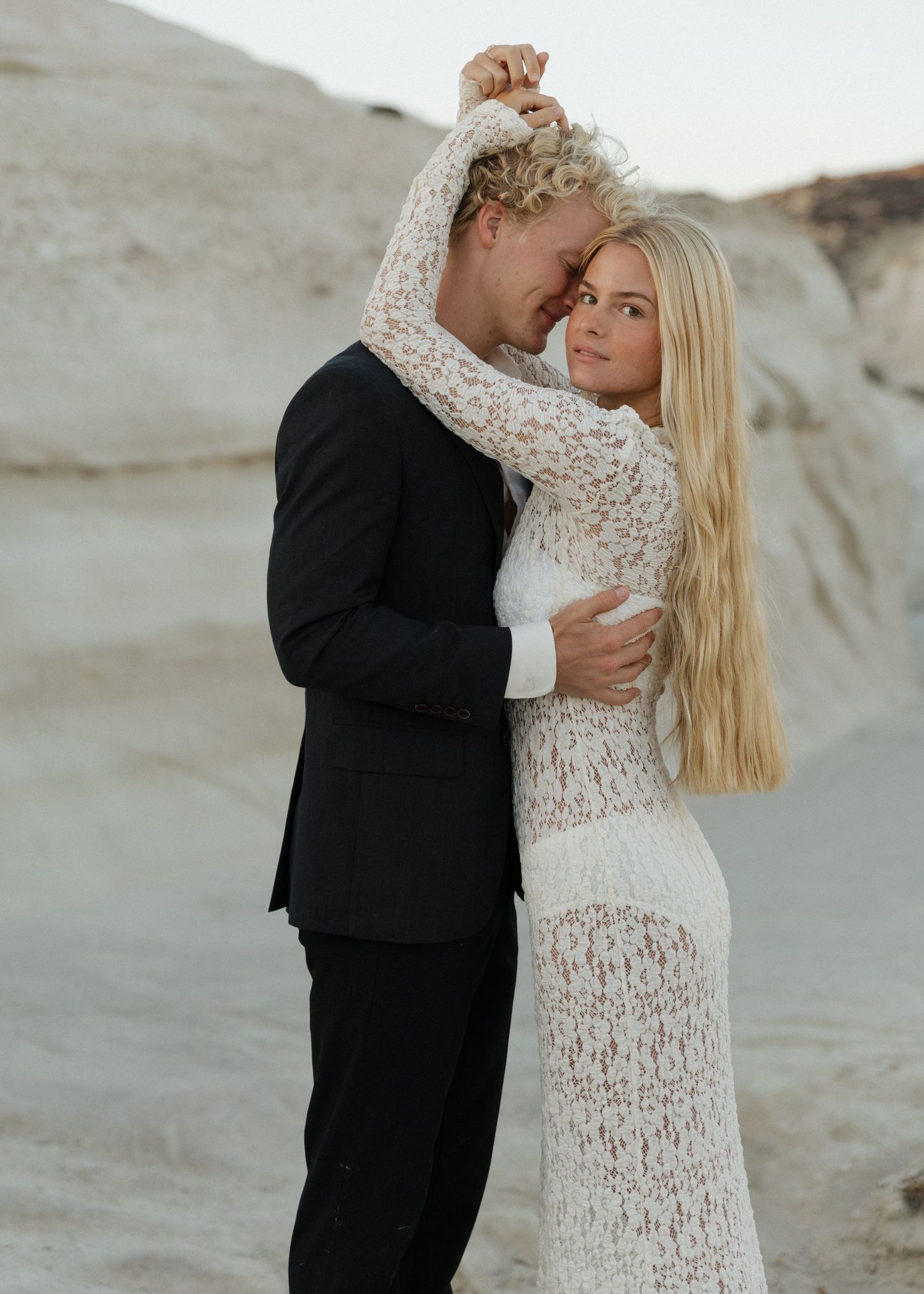 Romantic bride and groom poses against the moonrock backdrop at Sarakiniko Beach in Milos, Greece in elegant wedding attire.