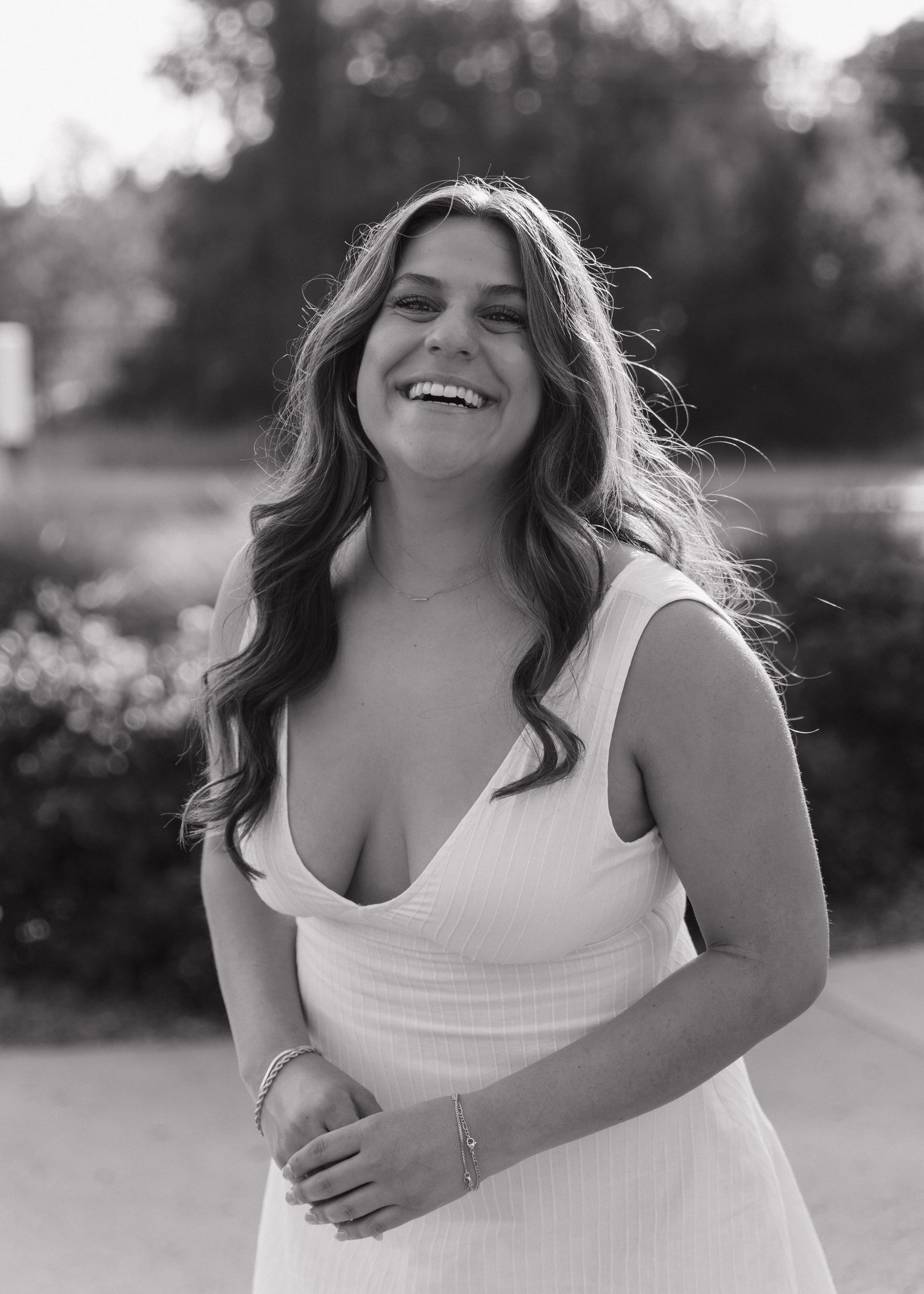 A Cal Poly San Luis Obispo graduate wearing a white dress laughs joyfully while posing outdoors in black and white photography.