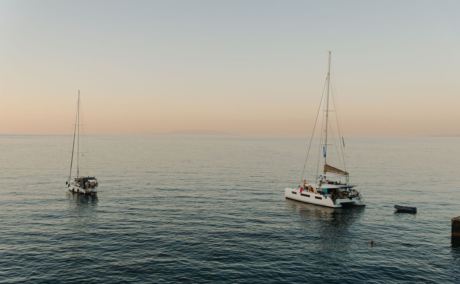 A series of boats sailing on calm mediterranean waters at sunset creates a peaceful panoramic seascape view in Milos, Greece.