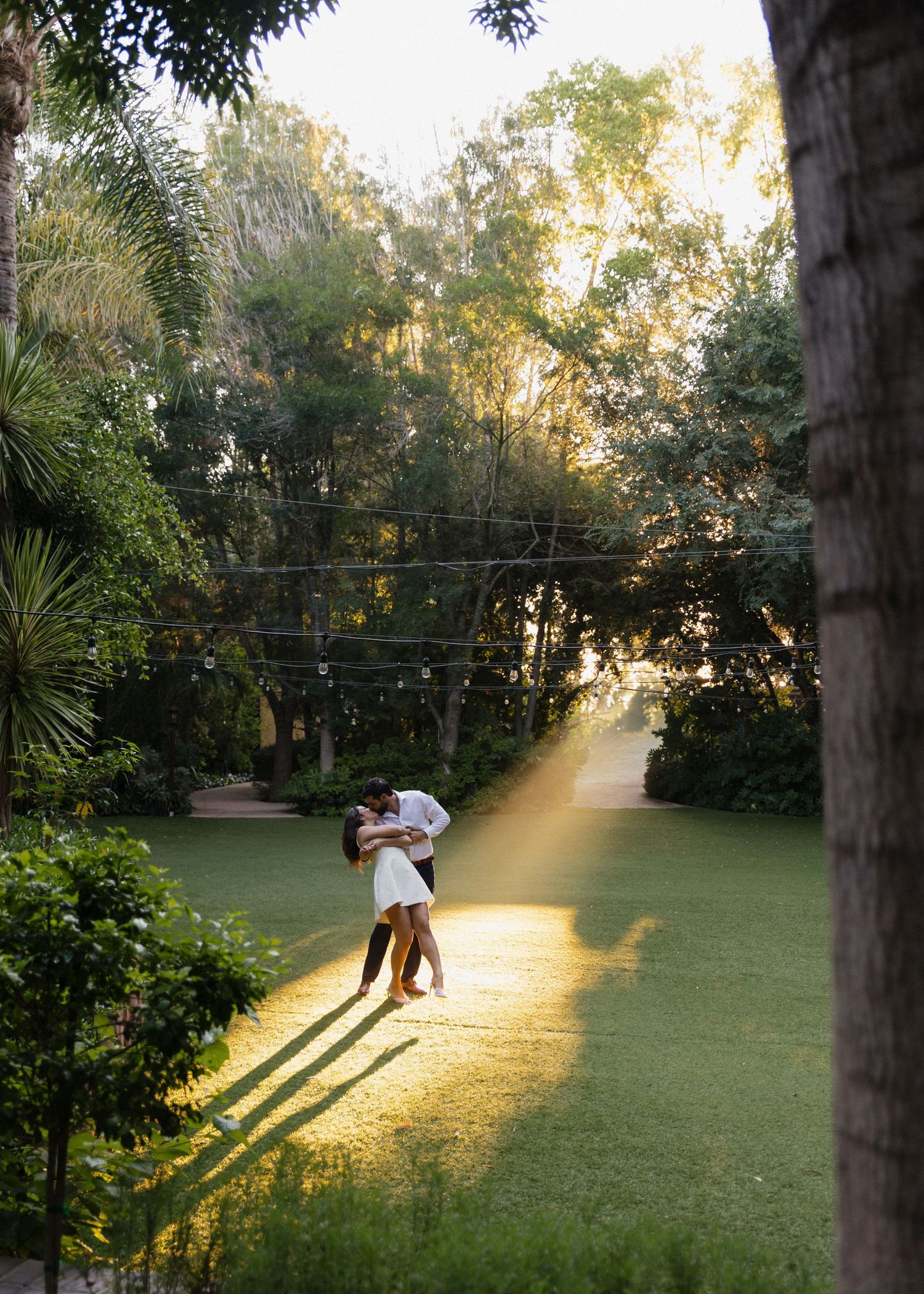 A romantic engaged couple dances together on a sunlit lawn at golden hour at Hartley Botanica in Camarillo, California.