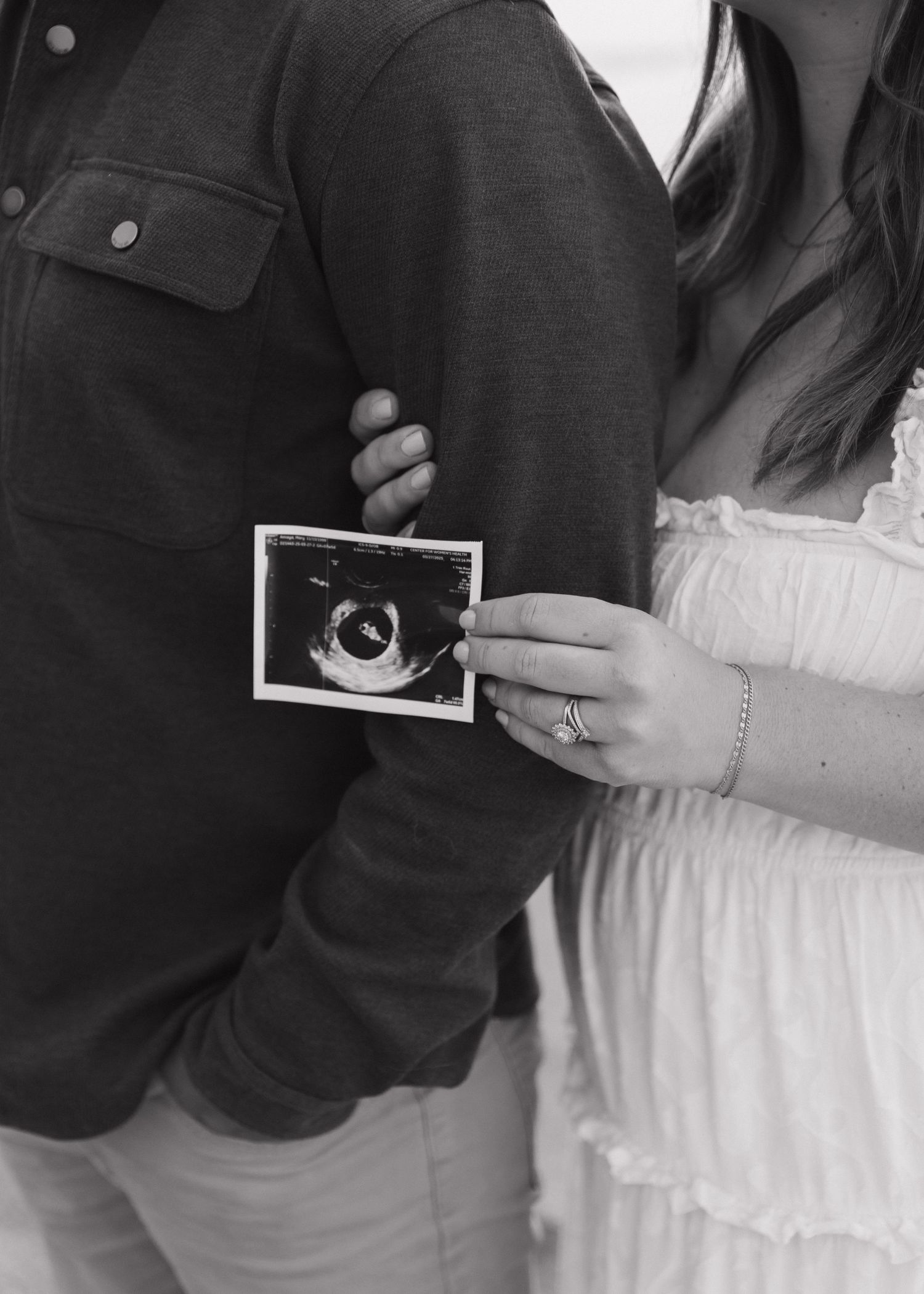 Close-up view of hands holding ultrasound photos against dark clothing.