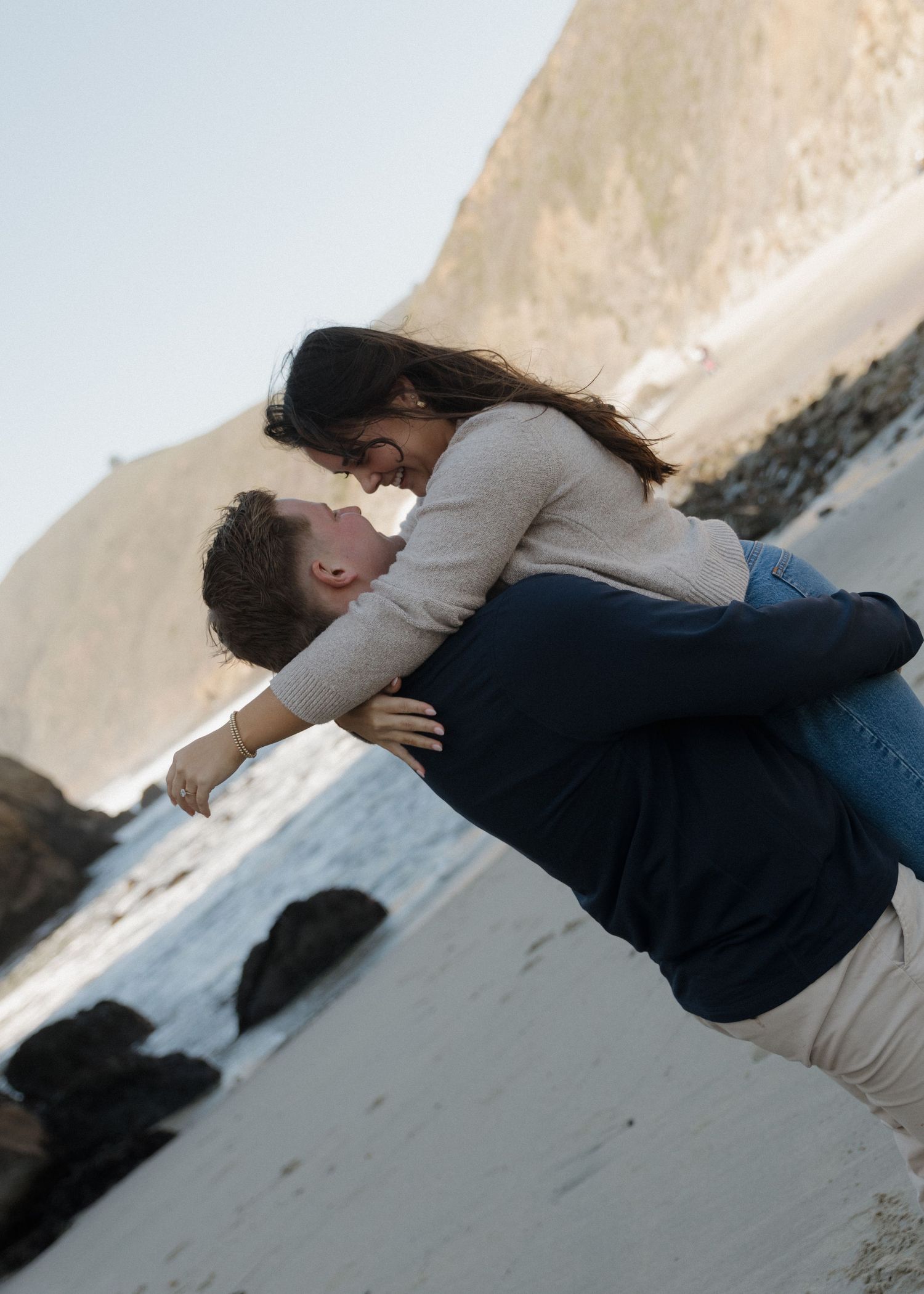 A freshly engaged couple embraces and spins at Pfeiffer Beach on the coast of Big Sur in California.