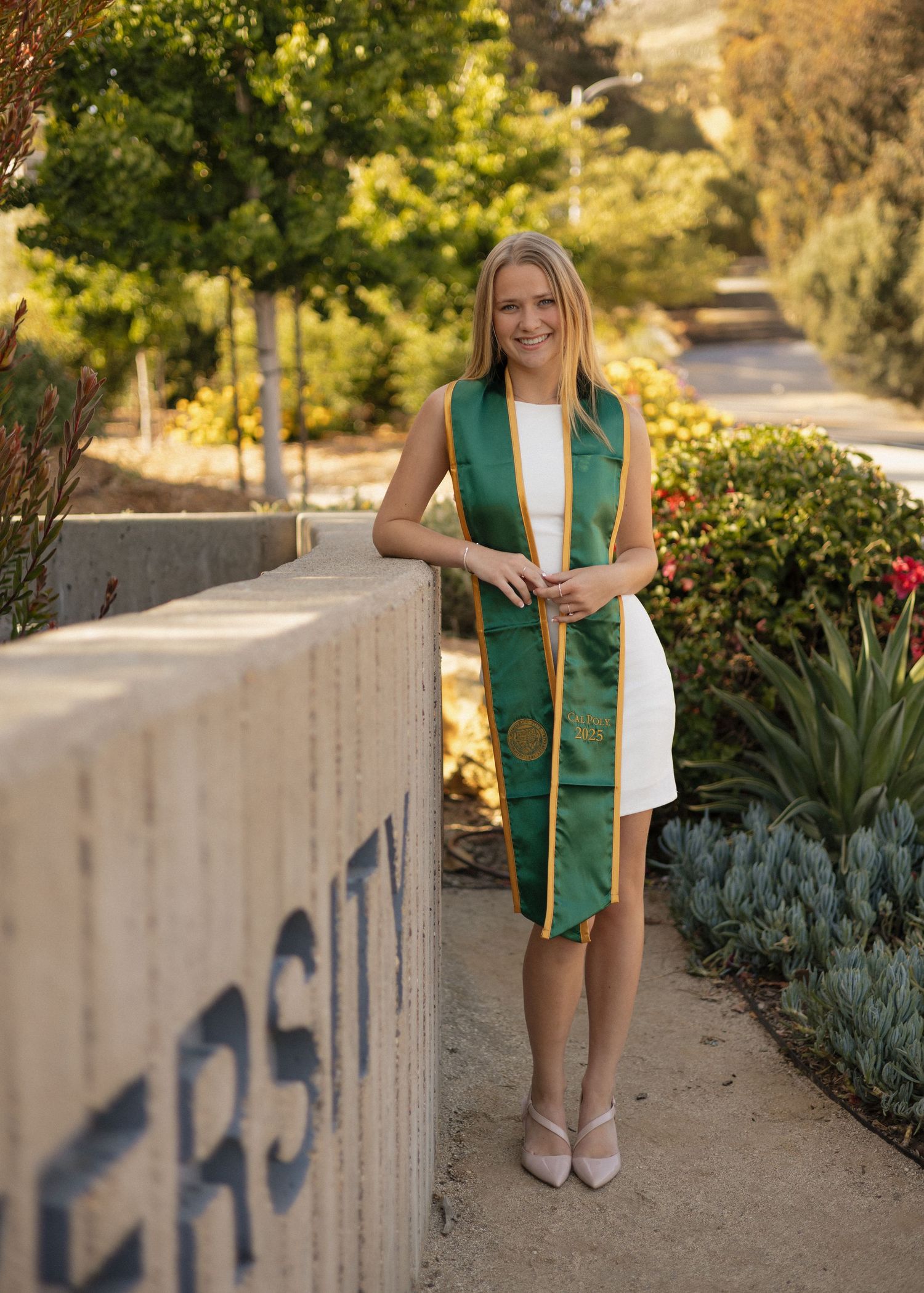 A Cal Poly San Luis Obispo graduate poses against the campus welcome sign in golden hour lighting.