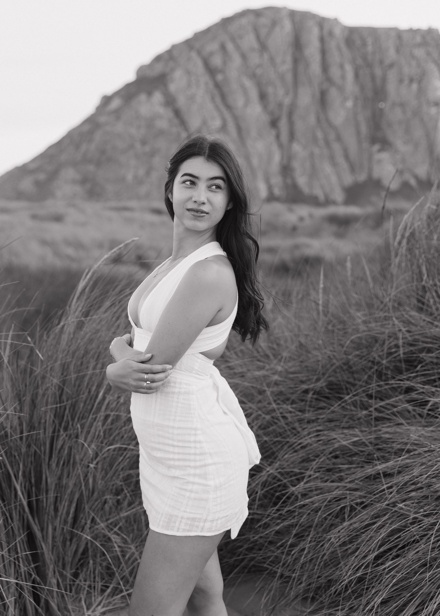 A woman in a white top poses playfully against a dramatic rocky landscape at sunset.