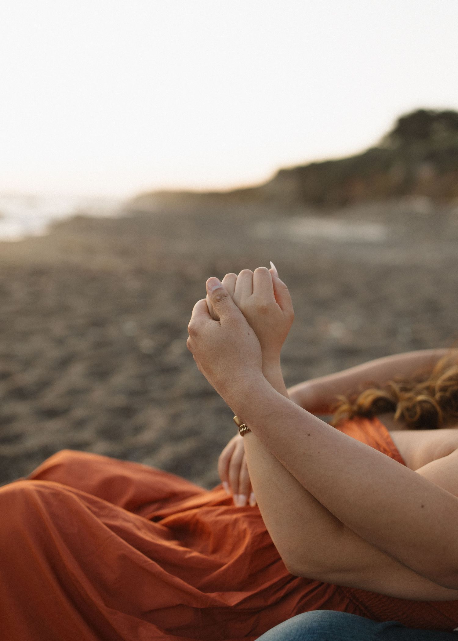 A close-up of a couple with hands clasped lying on a beach at sunset at Moonstone Beach in Cambria, California.