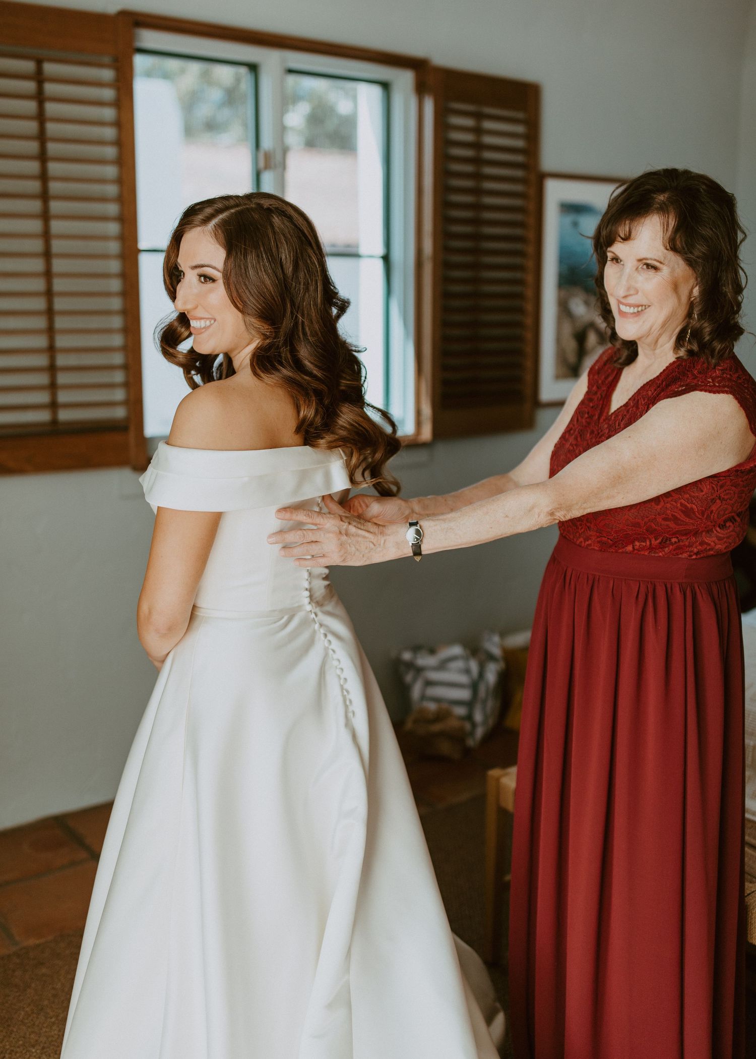 A bride's mother helping her into her white off-shoulder gown.