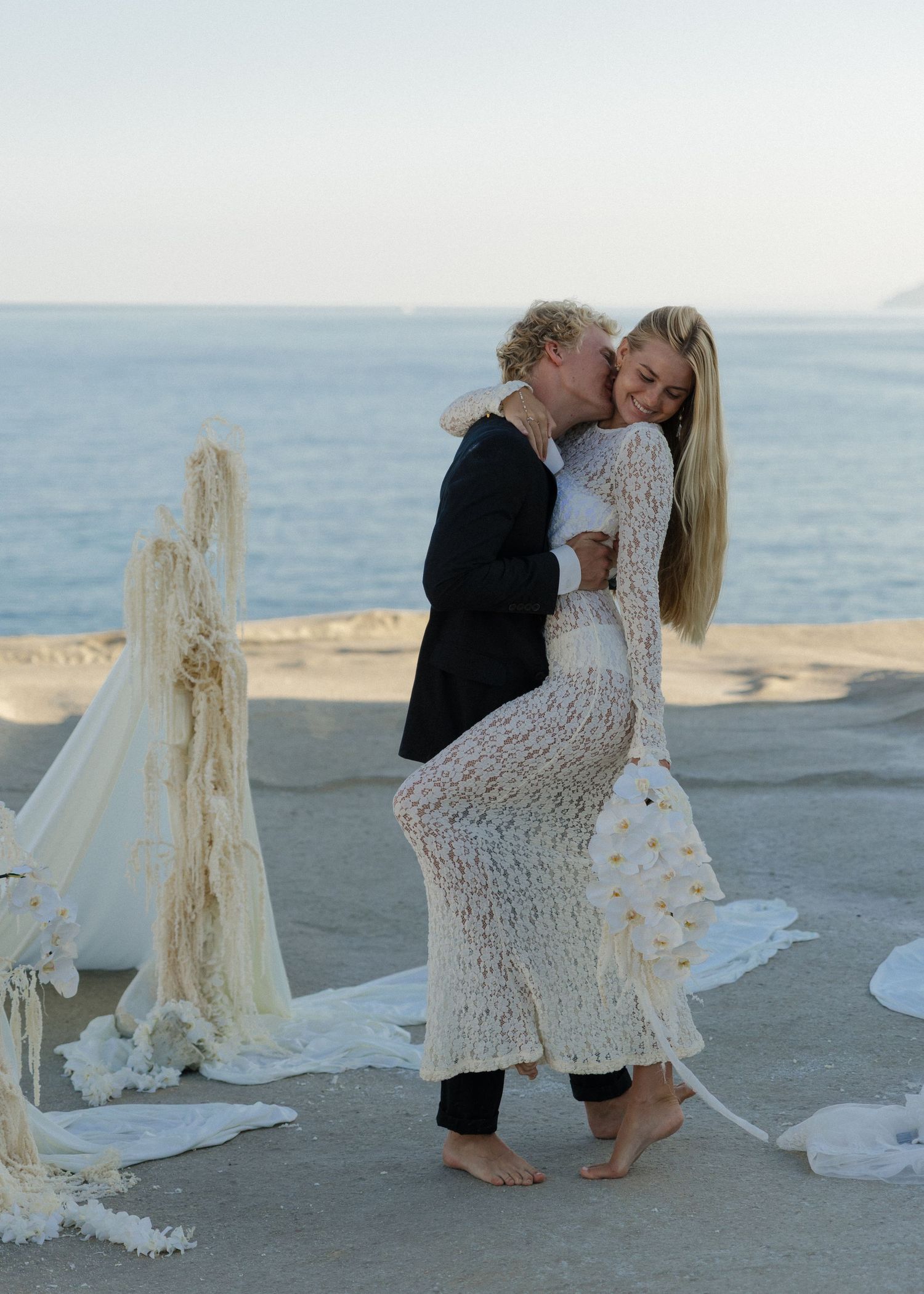 A romantic couple just married embraces after their kiss on a cliffside elopement at Sarakiniko Beach in Milos, Greece at sunrise.