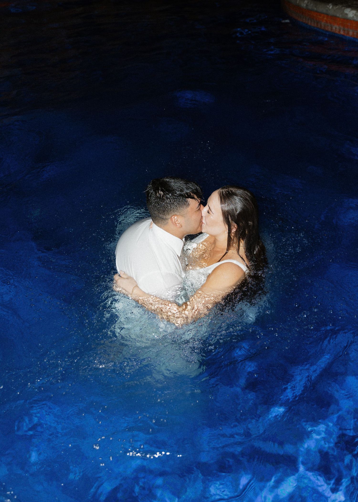 A soaking wet bride and groom share a romantic kiss in a dark blue illuminated pool at an intimate wedding in Puerto Vallarta, Mexico.