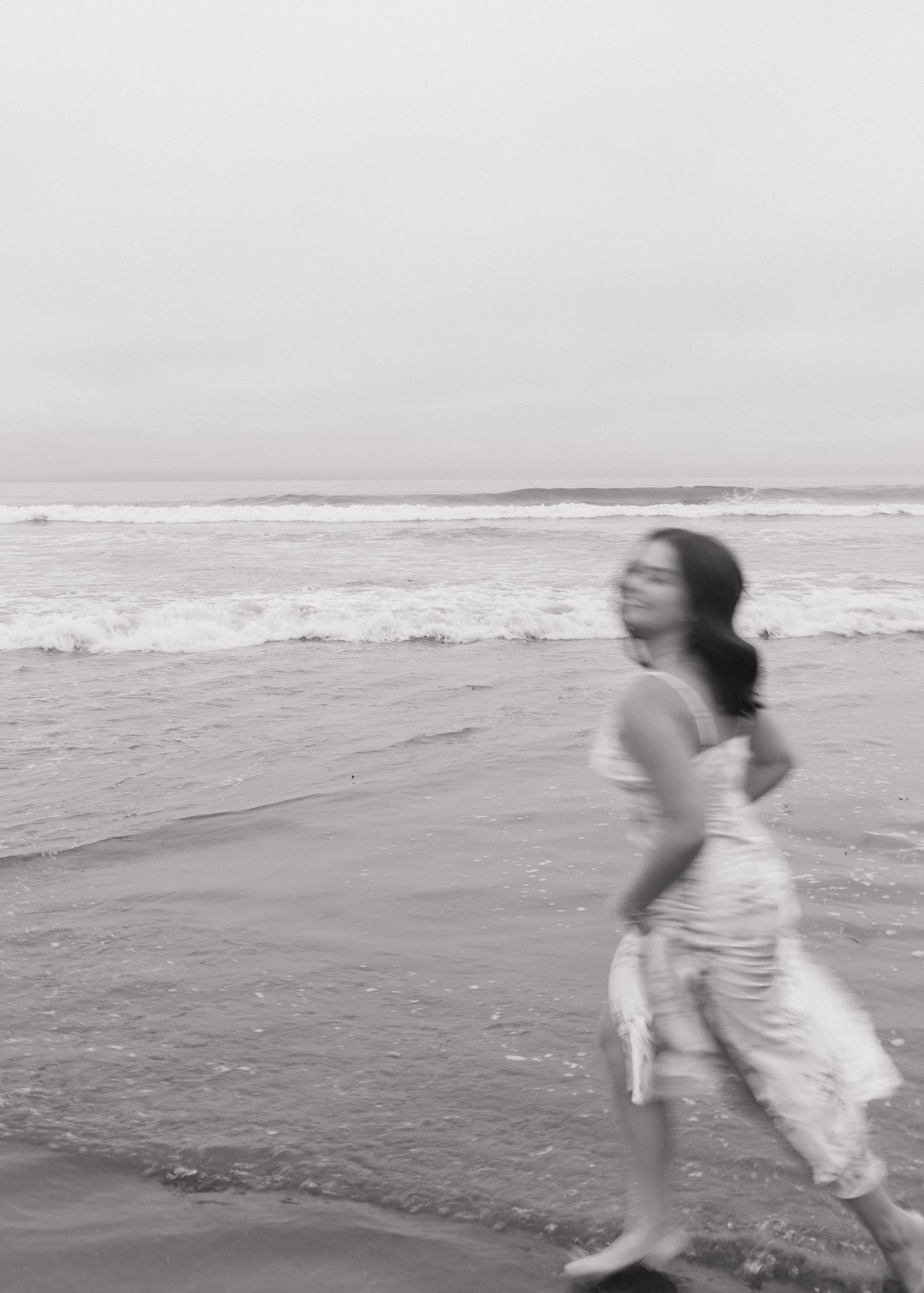 A blurry black and white photo shows a graduate running at the beach in Cayucos, California with ocean waves in the background.