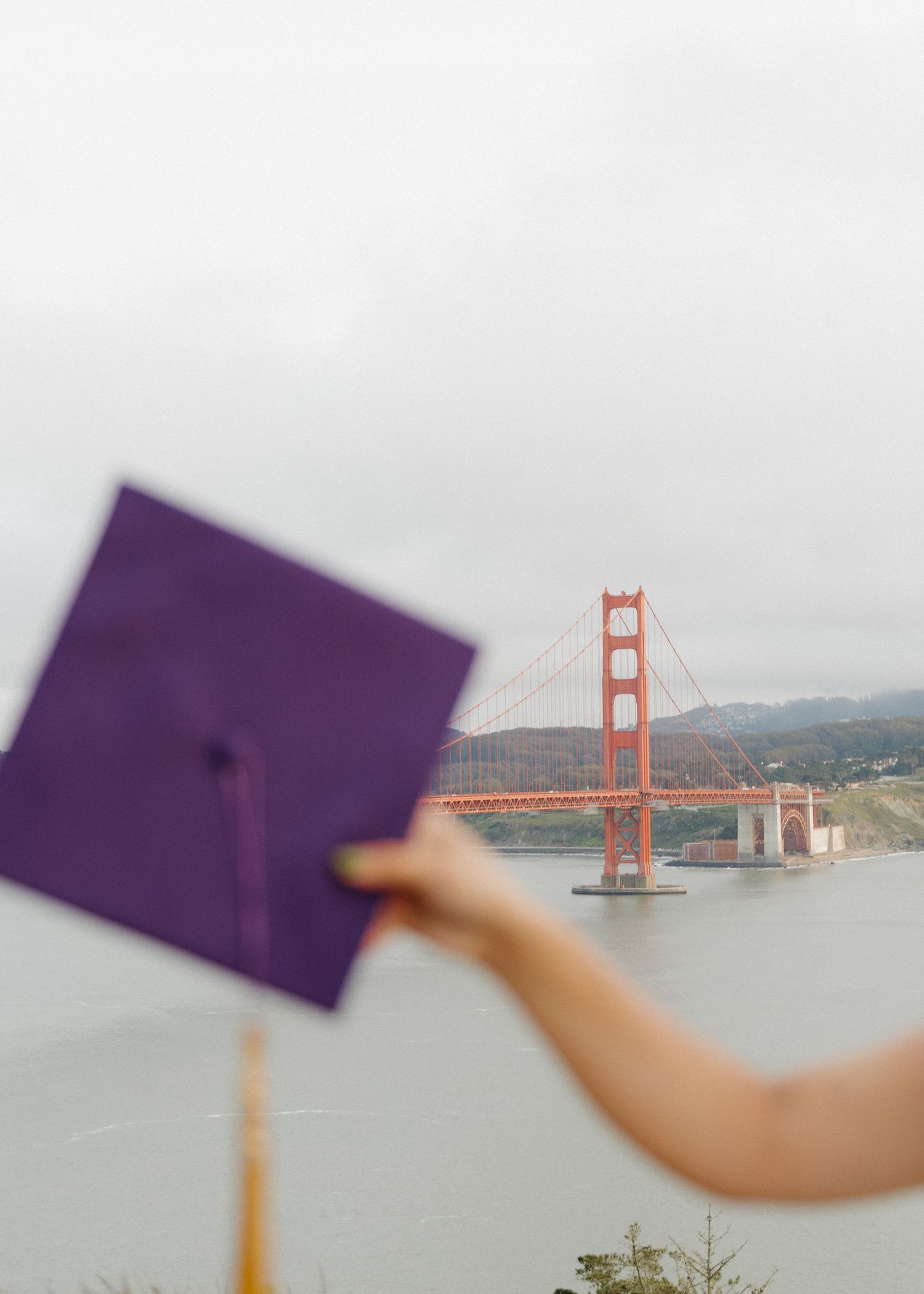 A San Francisco State University graduate holds her purple cap up with the Golden Gate bridge in the backdrop.