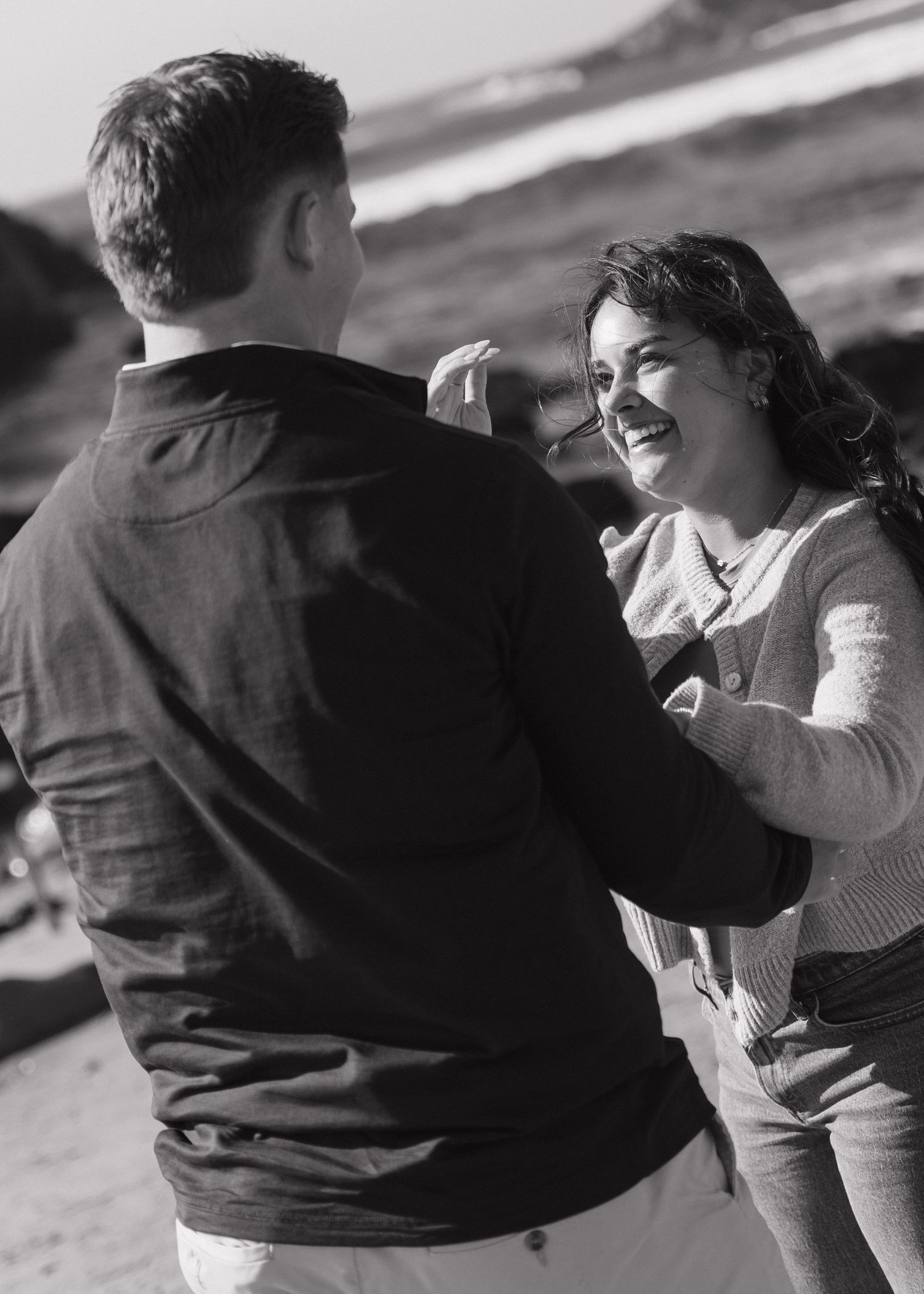 A black and white photo showing a freshly engaged couple smiling in celebration in Big Sur, California.