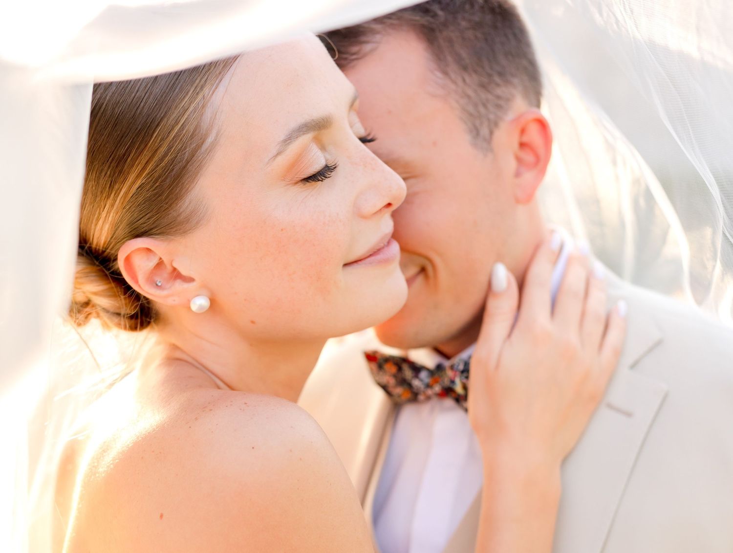 A tender romantic moment between newlyweds sharing an intimate embrace under a sunlit veil.