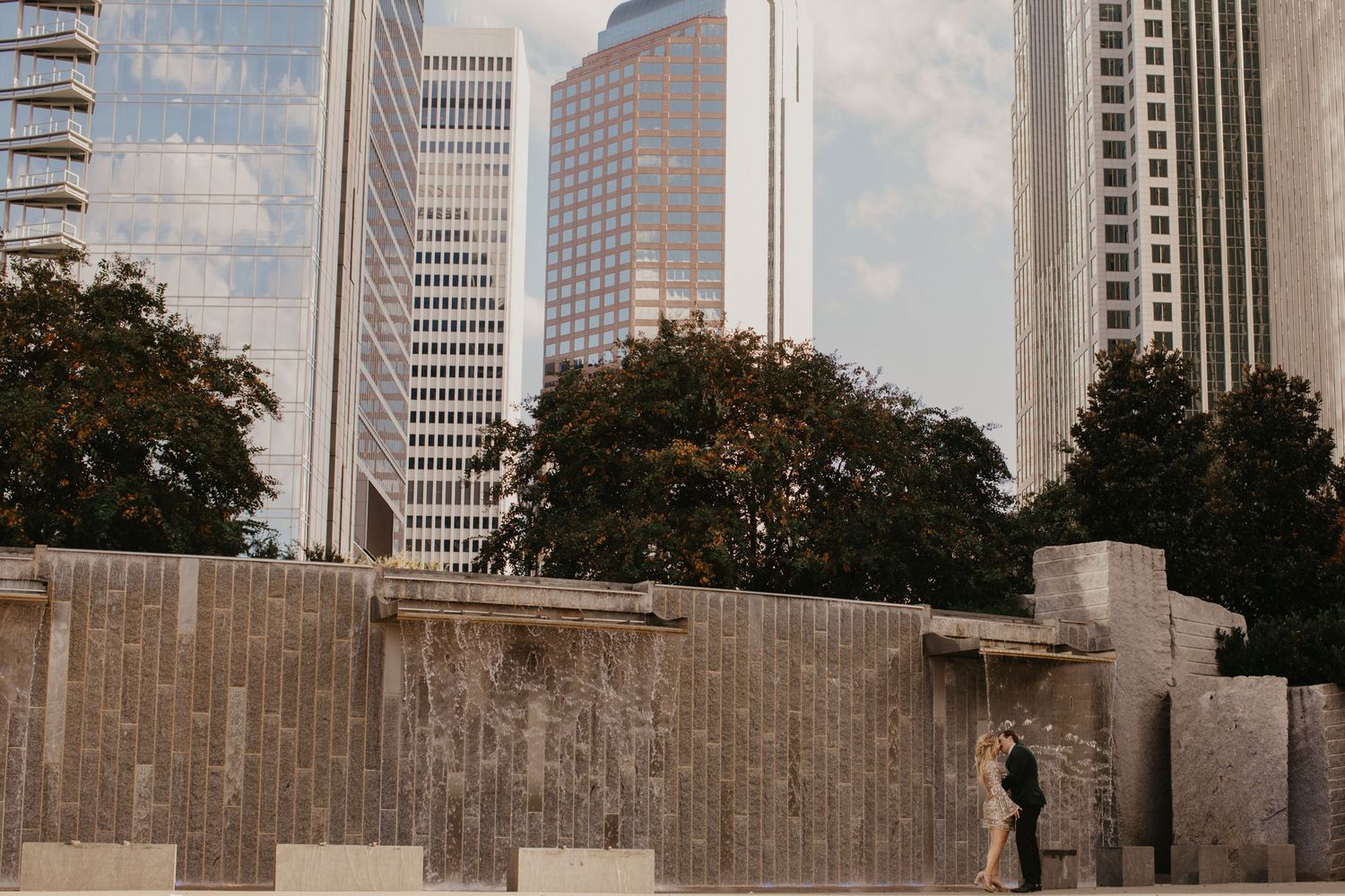 Urban scene with concrete wall and modern glass skyscrapers in downtown area with trees in the background in Charlotte
