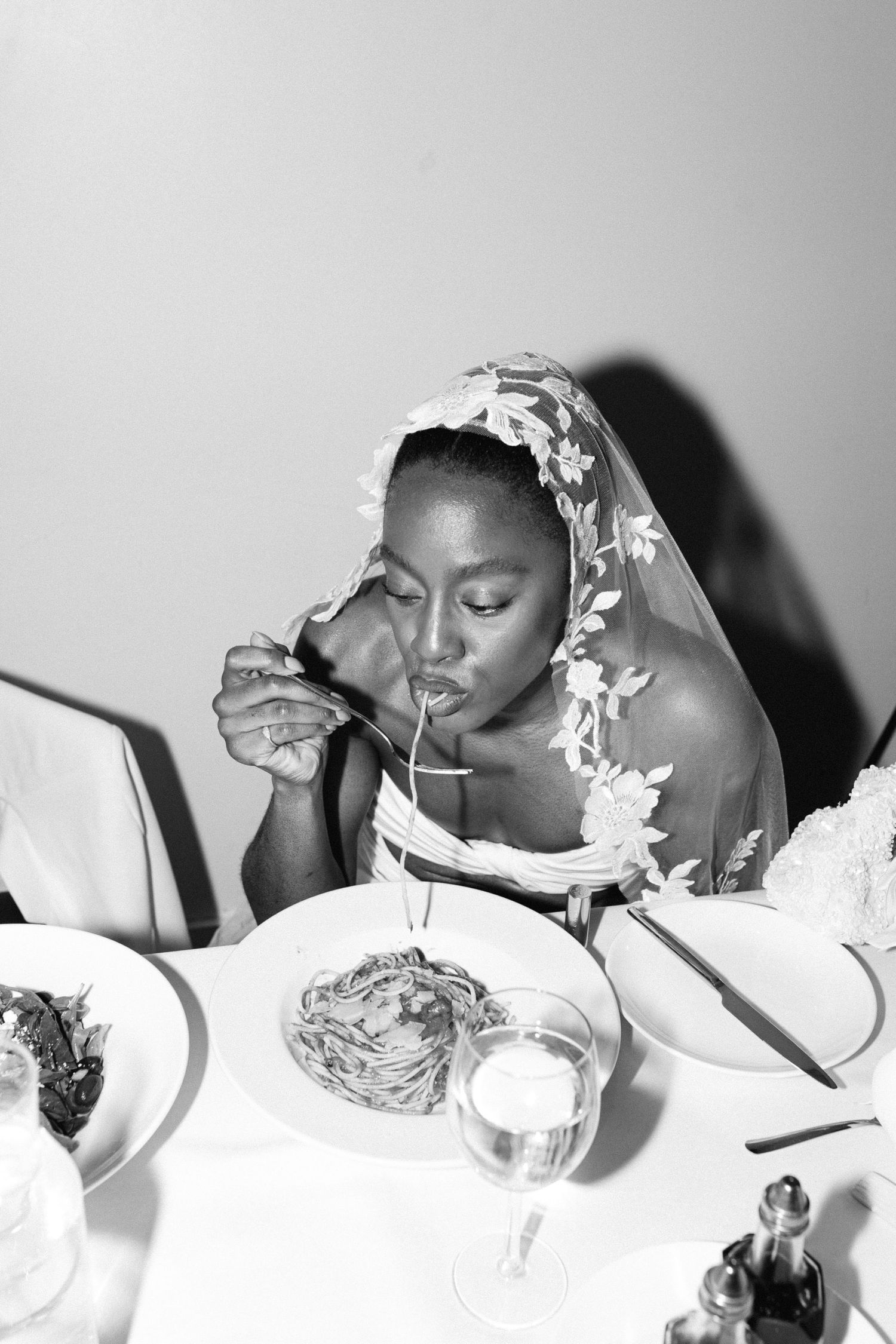 Black and white photo of bride wearing floral veil eating at wedding reception.