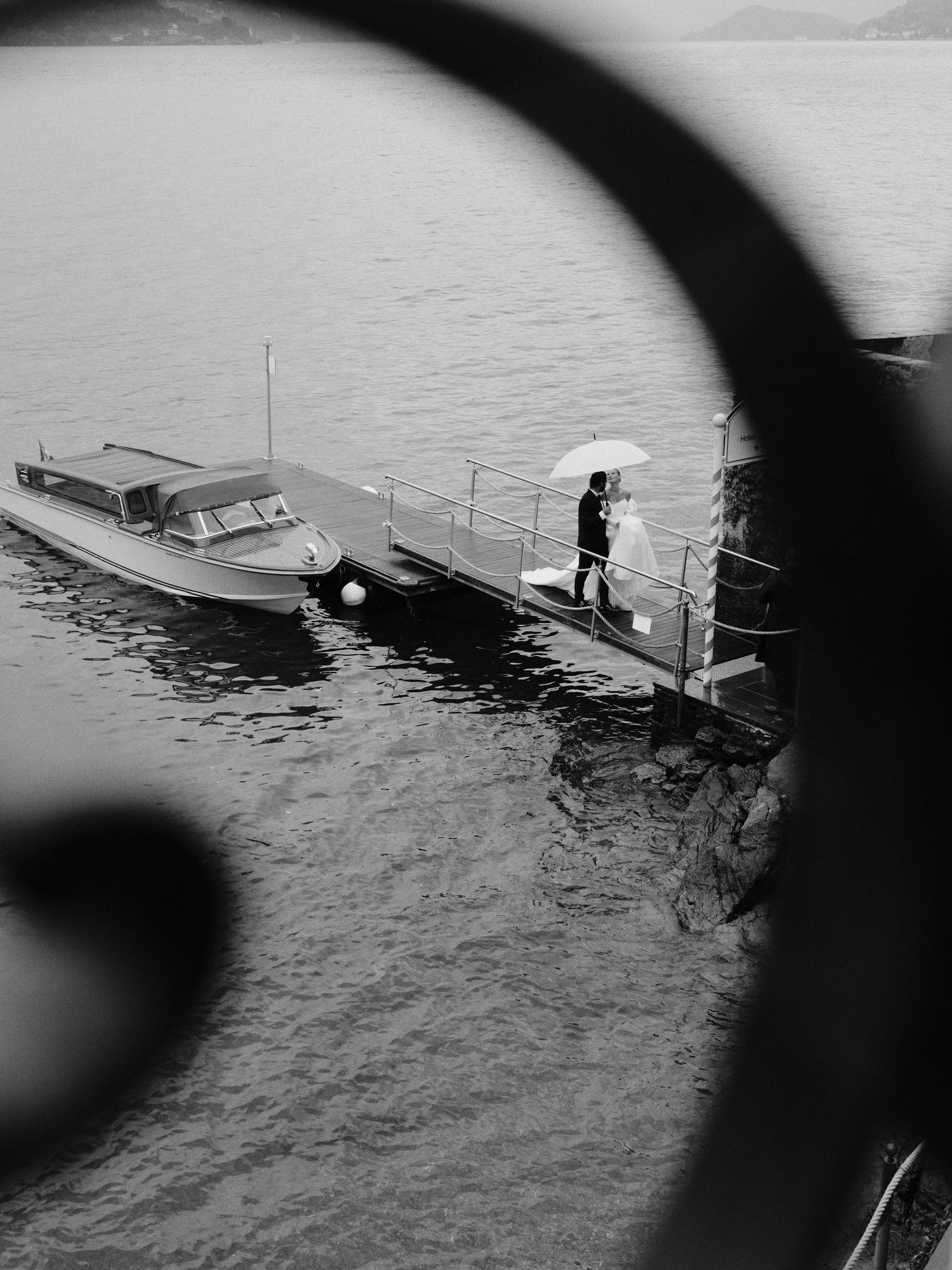 A black and white view of a person walking on a dock with a boat in misty water.