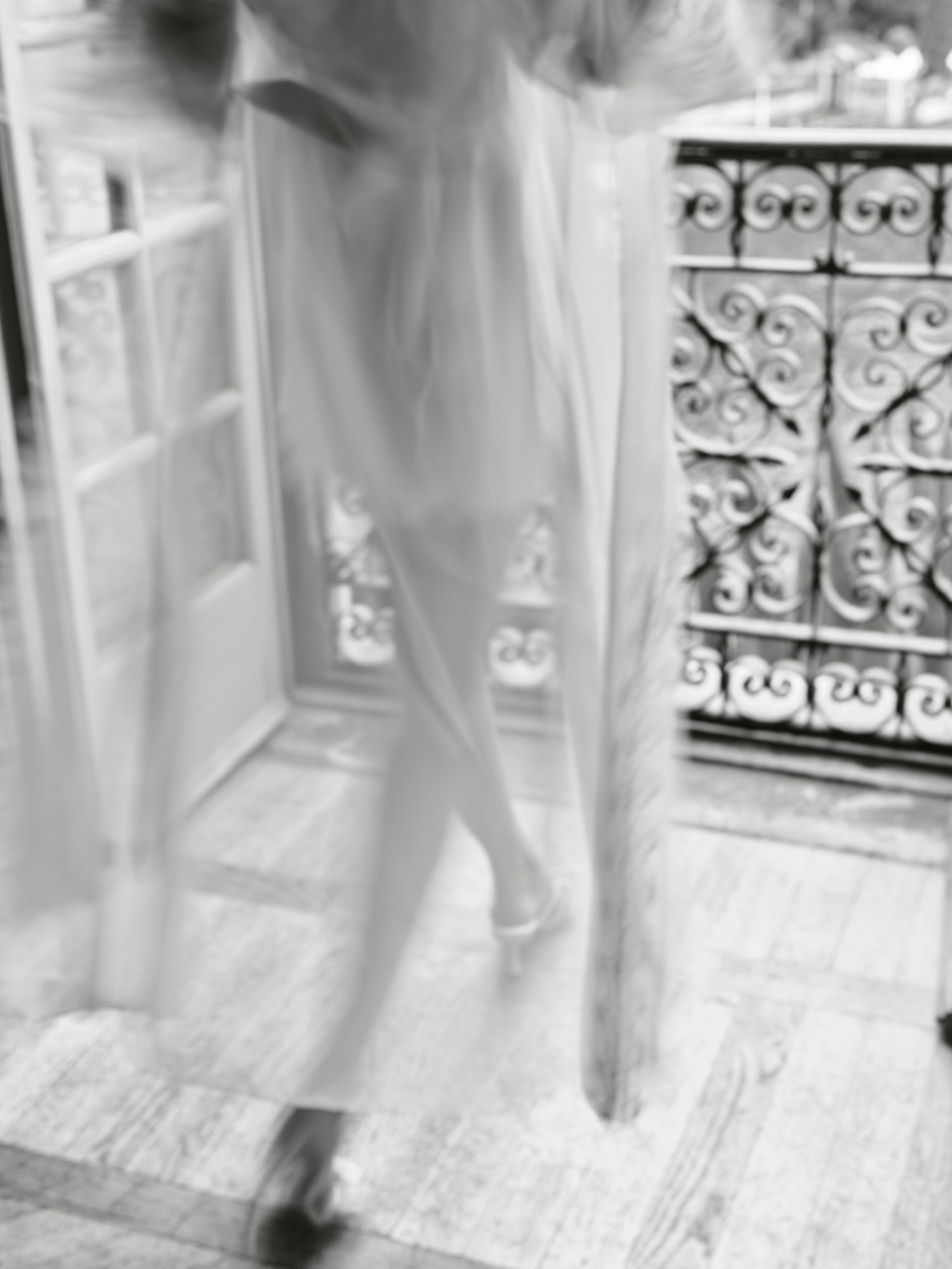 Ethereal black and white photograph showing a blurred figure near an ornate wrought iron balcony railing.