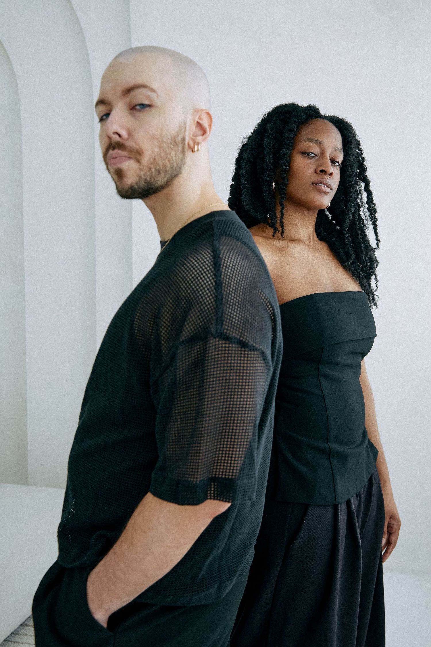 Fashion portrait of couple in black outfits against white minimalist background.