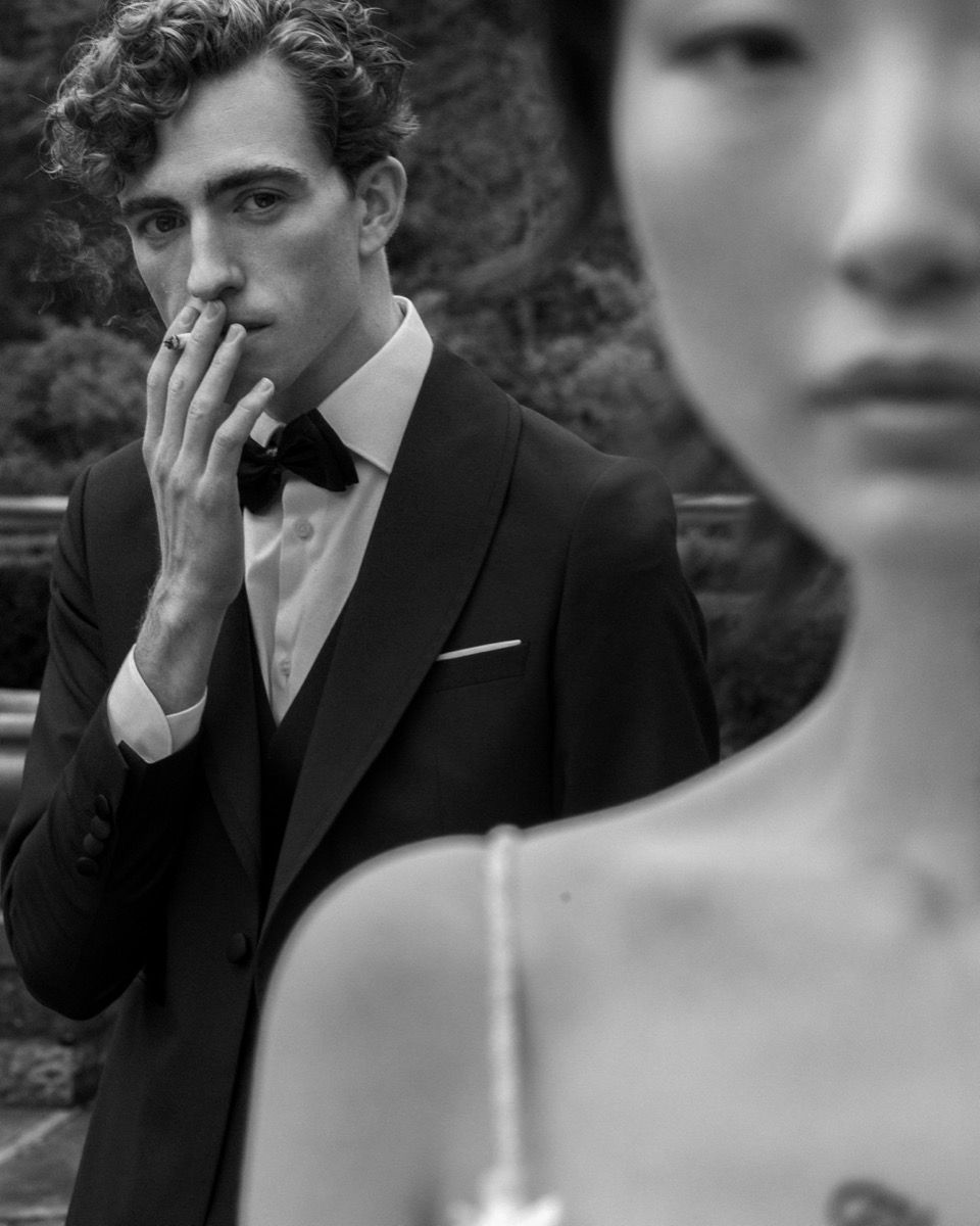 Artistic black and white portrait of couple with groom smoking in formal attire.