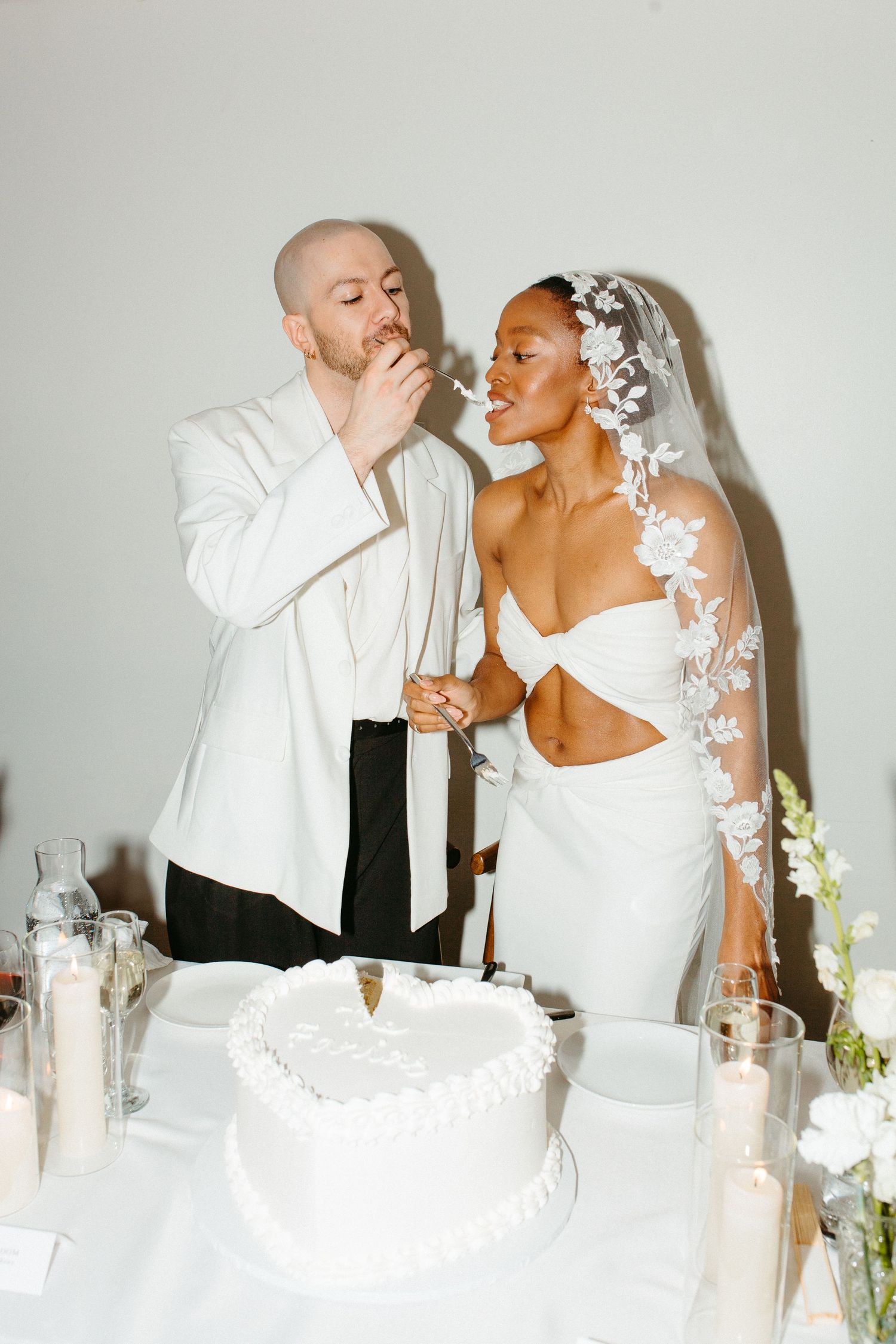 Newlyweds share a playful moment while cutting their white wedding cake at the reception.