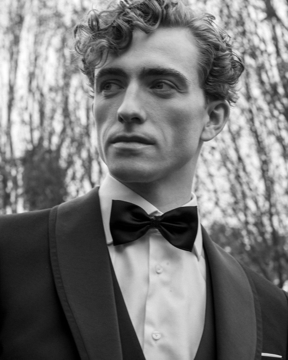 Formal black and white portrait of man in tuxedo and bowtie looking to the side.