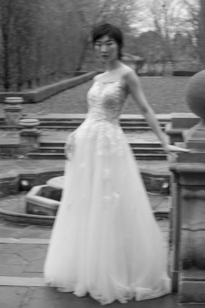 Vintage black and white photo of person in flowing wedding gown outdoors.