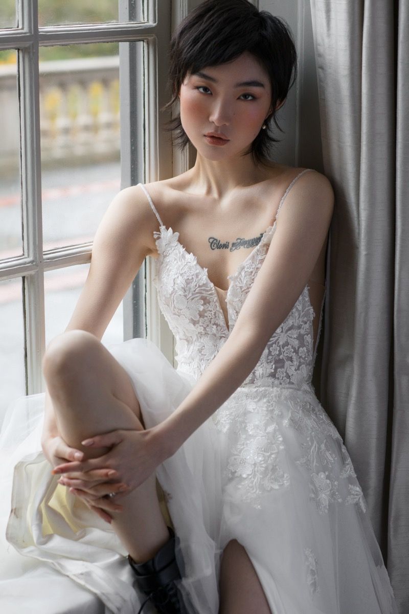 Wedding dress with lace details and leg slit photographed by window.